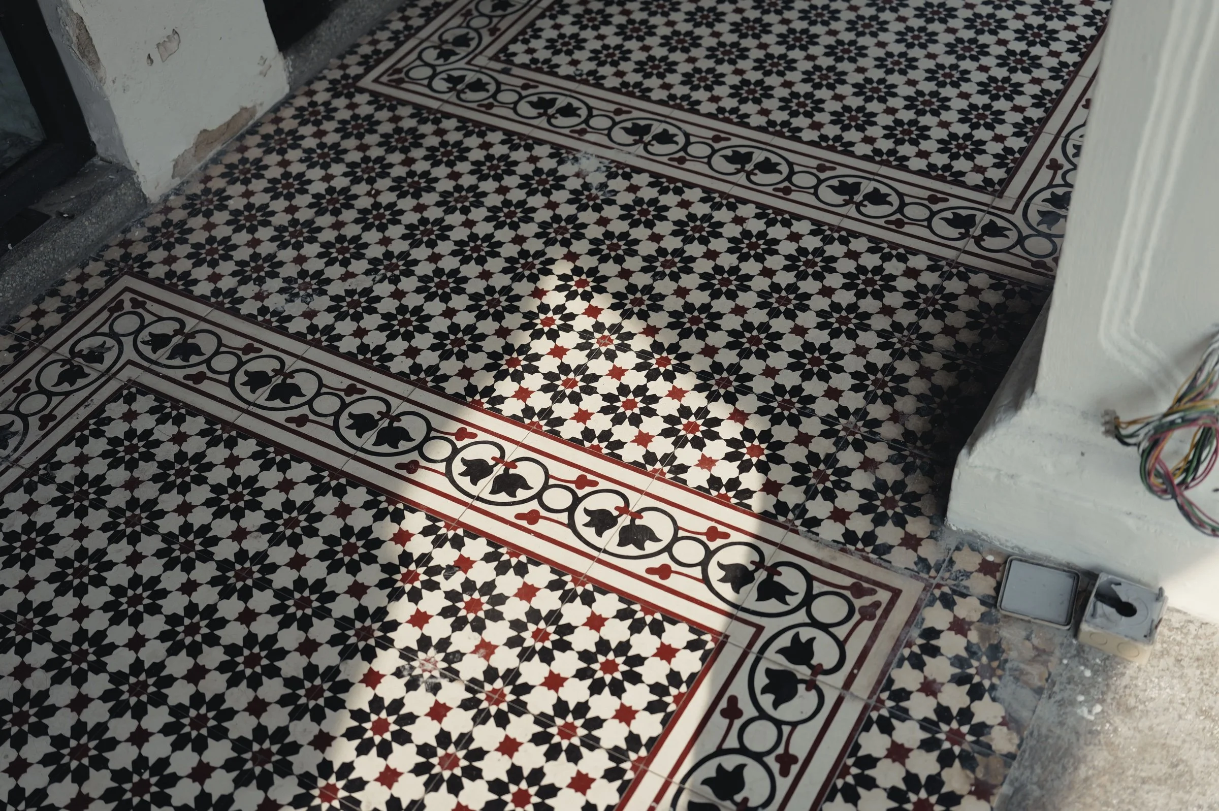 Sunlight falls across patterned red black and white floor tiles.