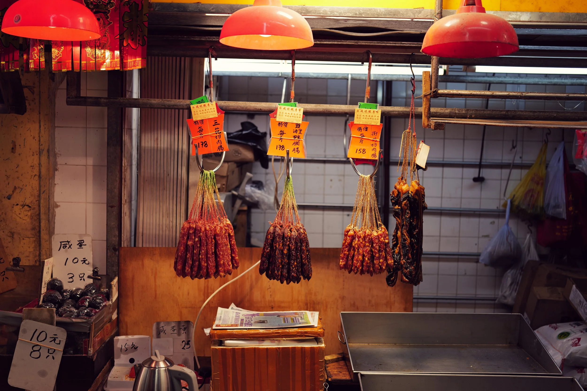 Hanging meats, like sausages, at a market stall, with handwritten price tags in Chinese characters.