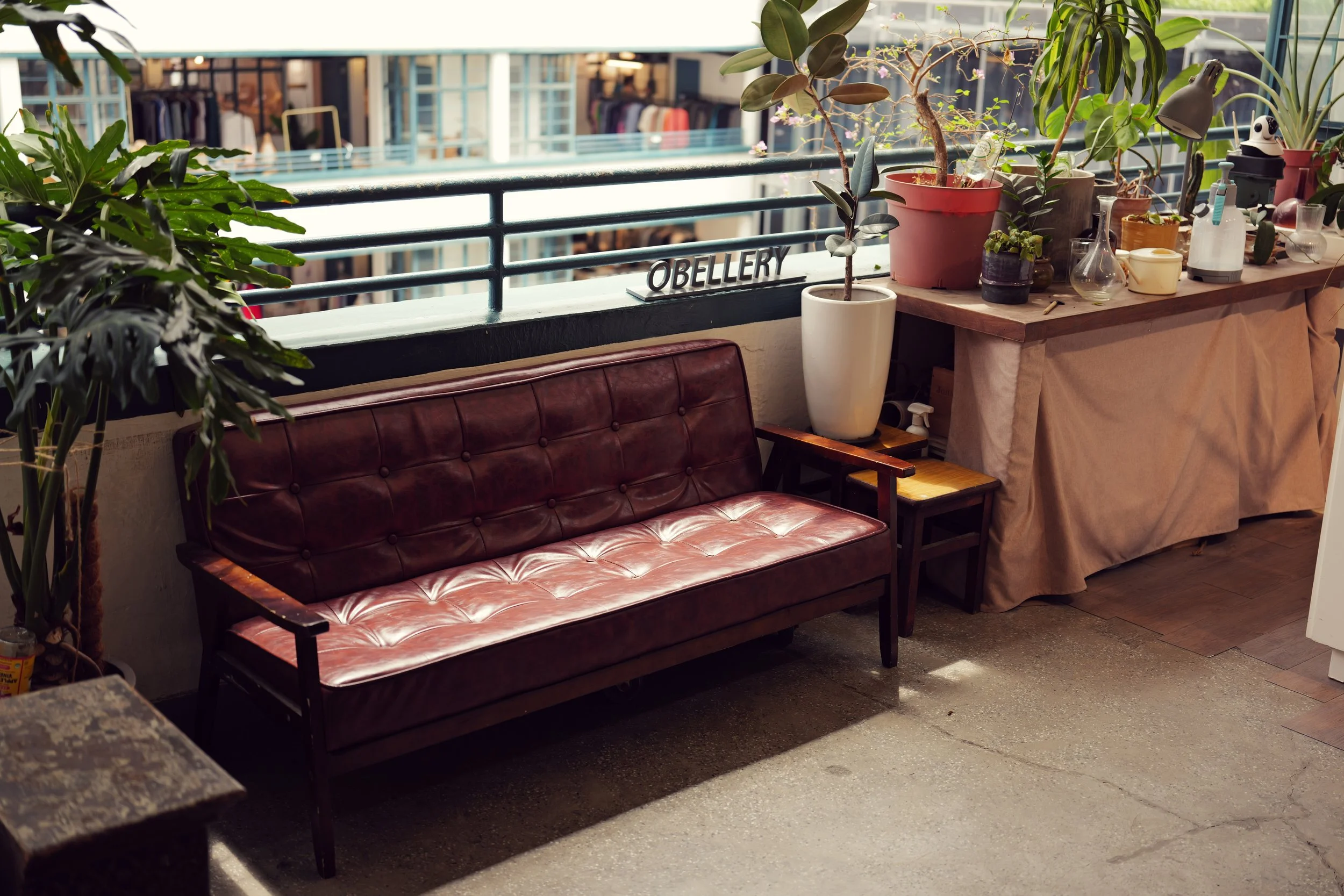 Indoor balcony with plant pots, a couch, and a workspace with plants, tools, and containers on a wooden table.