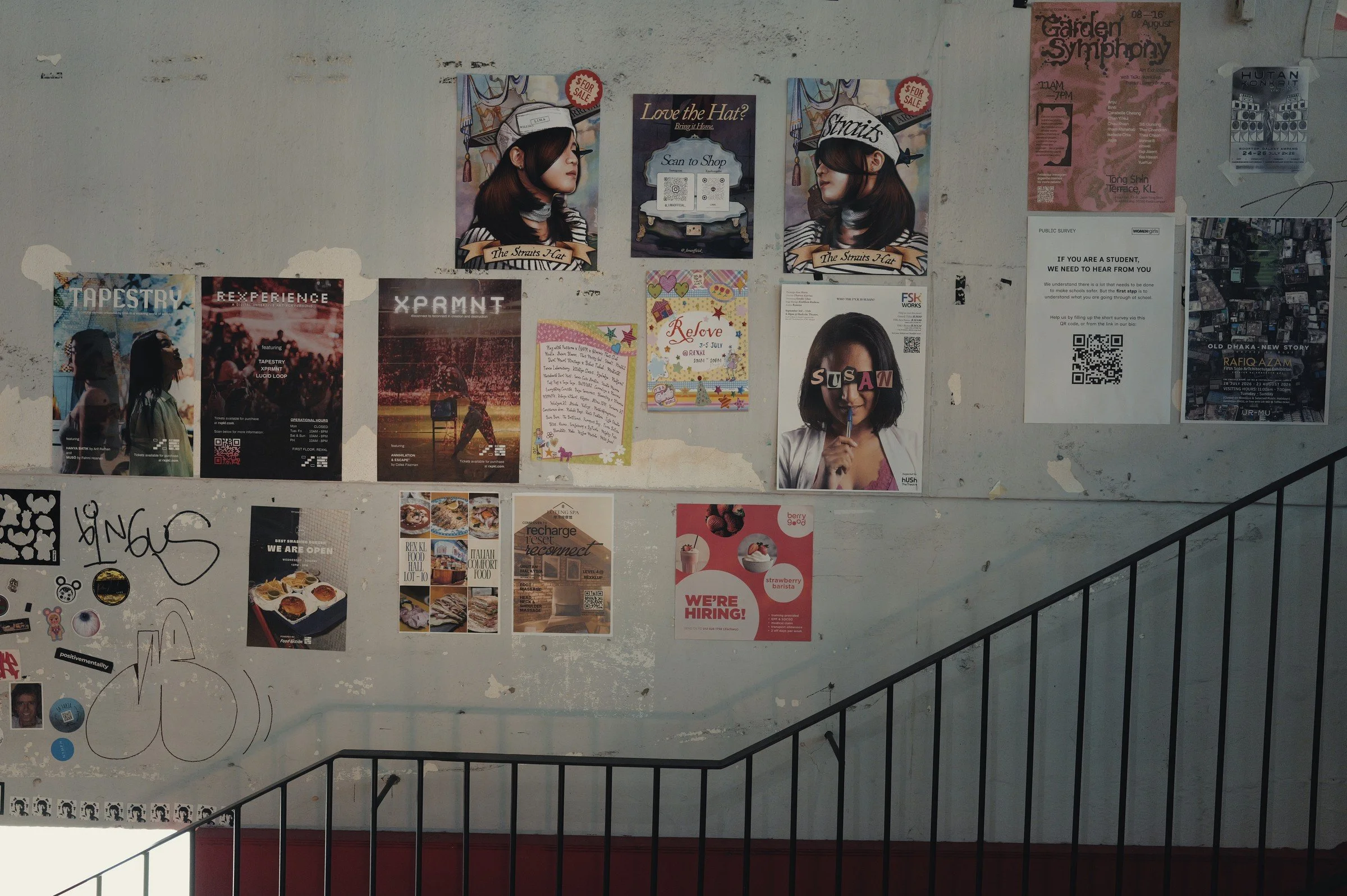 Posters cover a pale wall above a descending black stair rail.