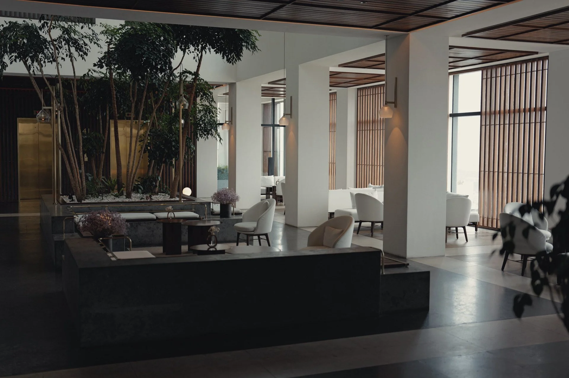 Light-filled lobby and dining area at Alila Bangsar, with white columns, wooden screens and greenery.