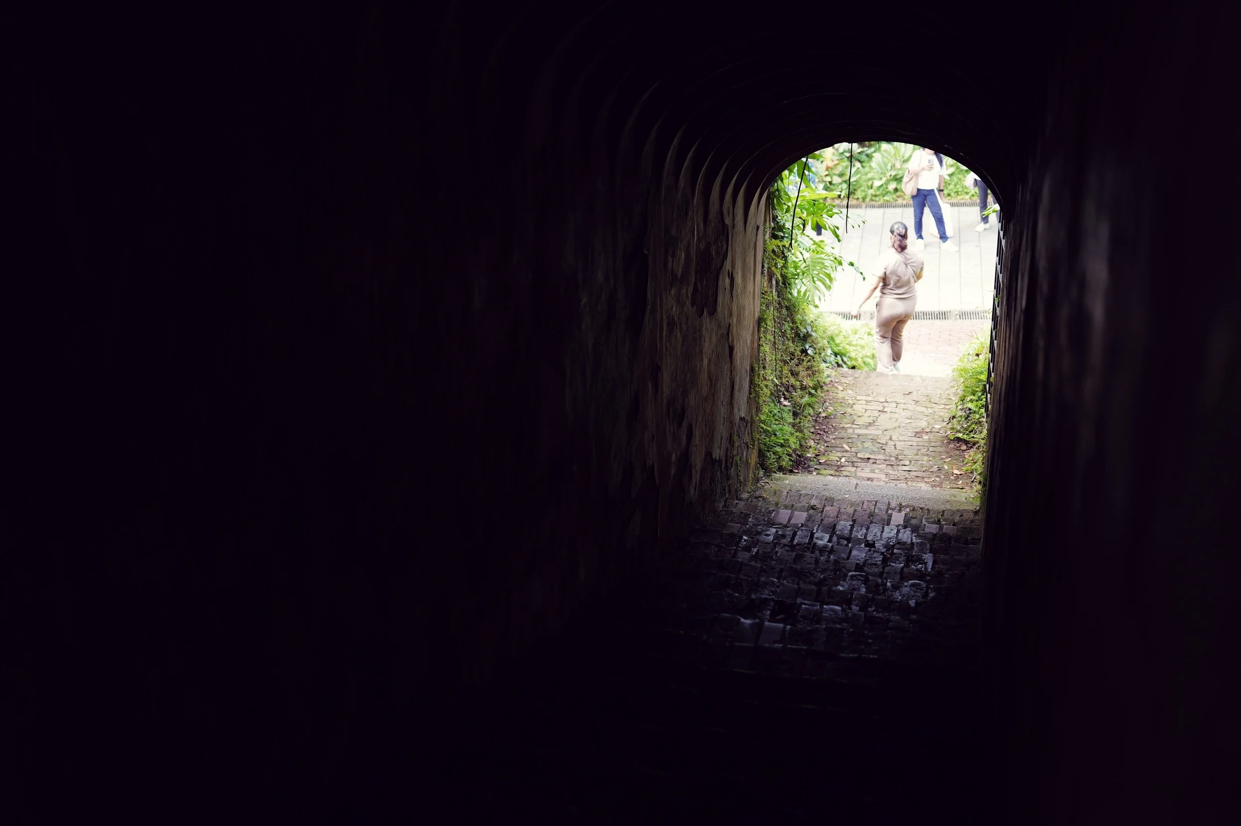 Daylight frames the end of a dark brick passage at Fort Canning Park, Singapore.