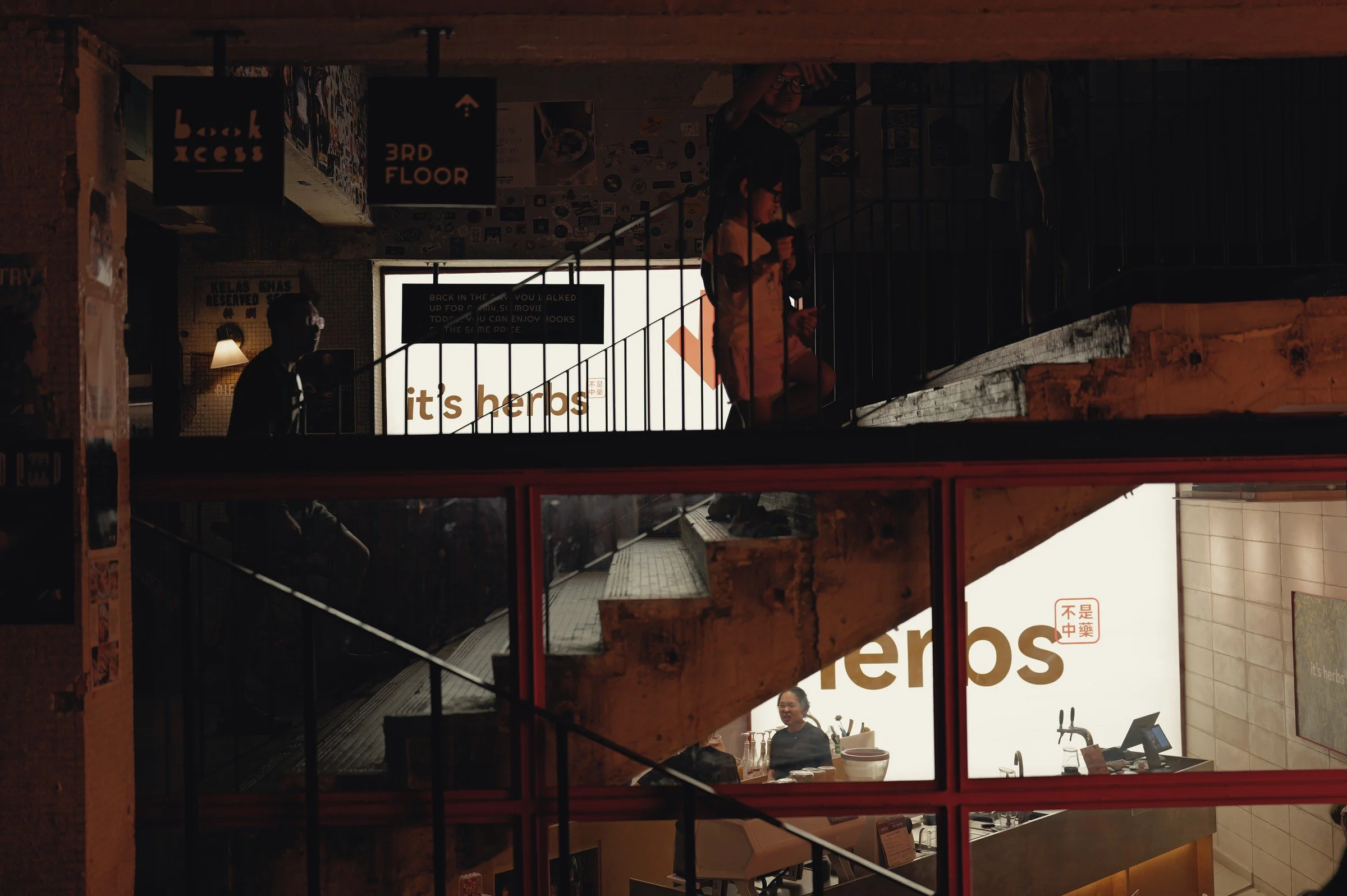 Warm light falls across an interior stairwell and layered shopfront signs.