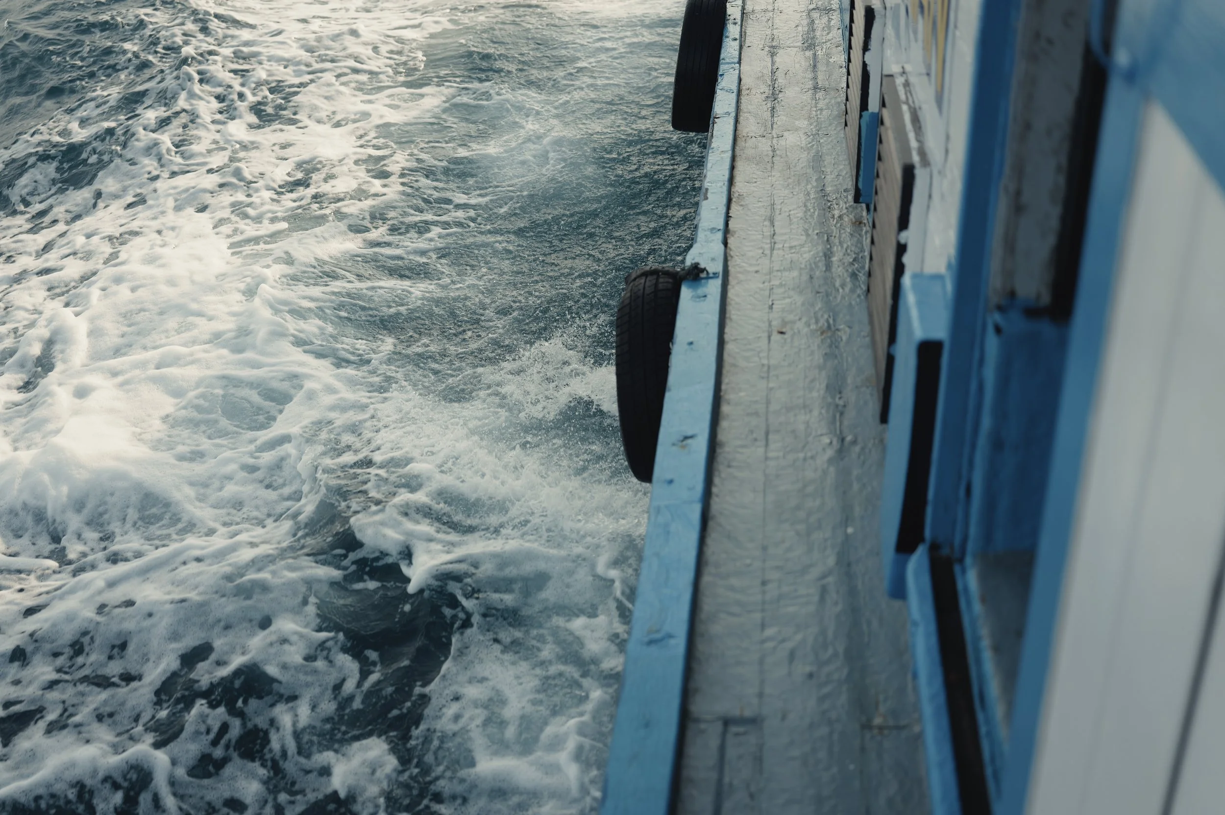 View from a boat showing the water surface with foamy waves and the side of the boat.