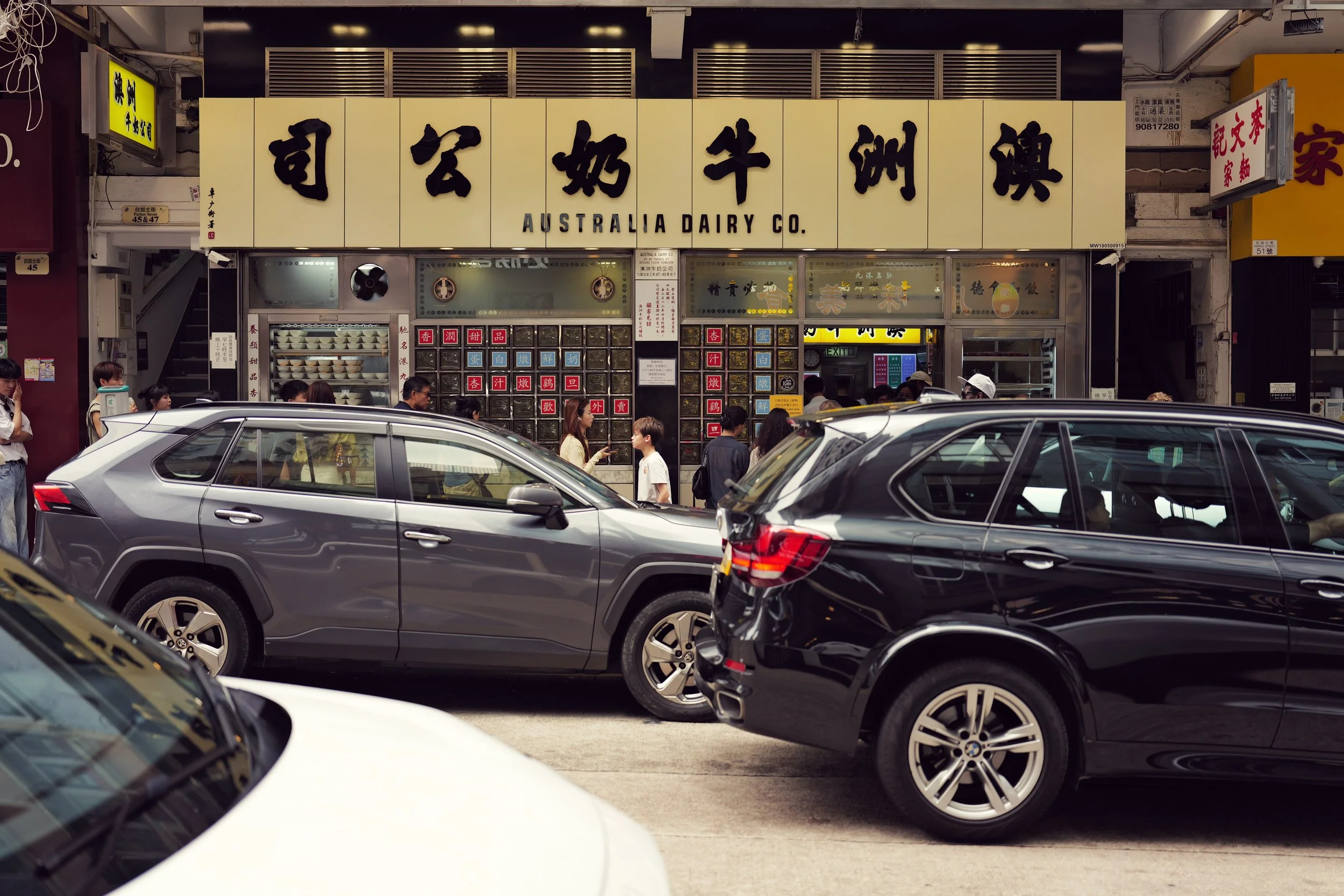 Street scene in front of Australia Dairy Co. restaurant with cars parked and people walking outside.