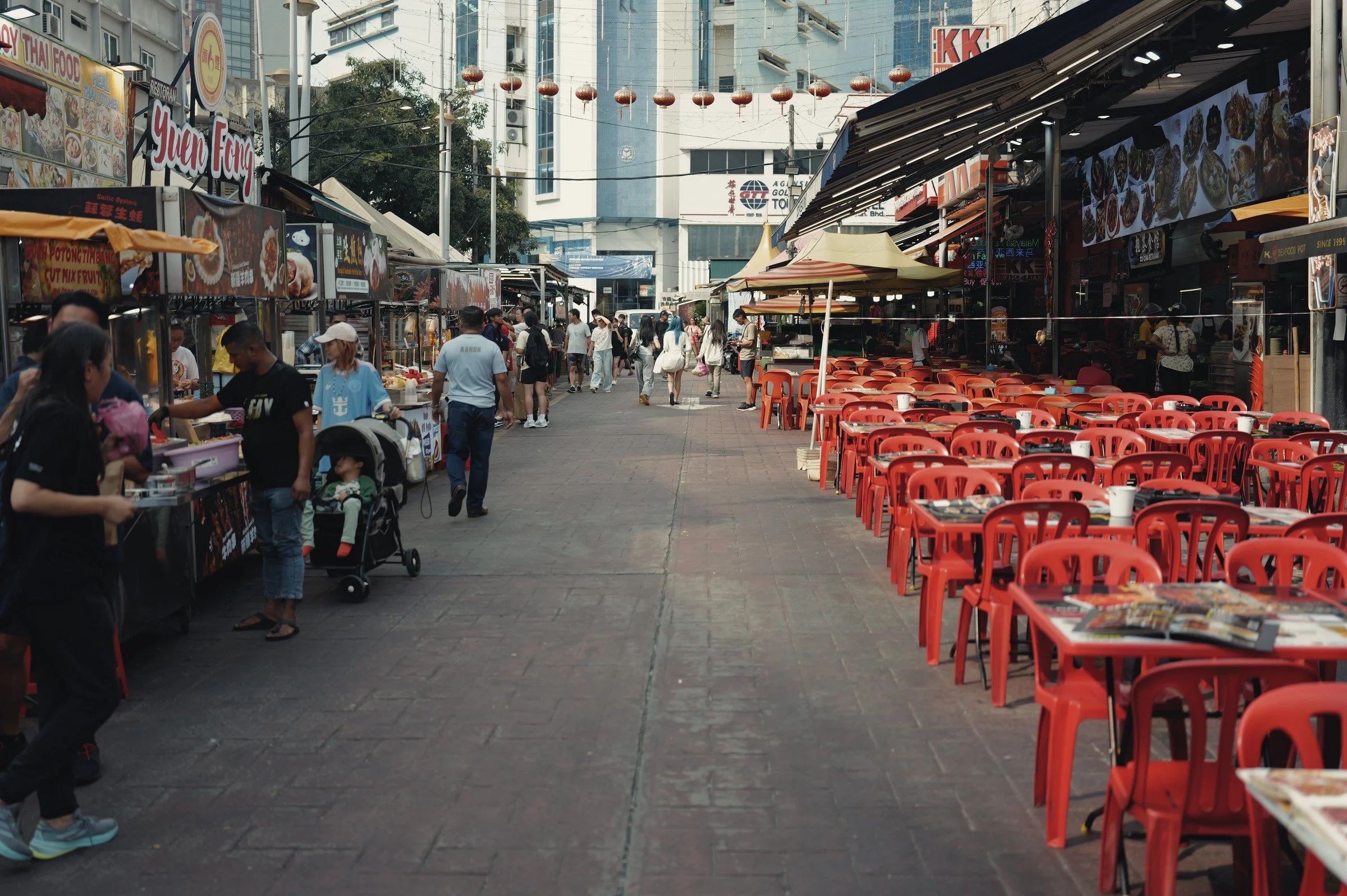 Rows of red chairs lead down an outdoor food street lined with stalls.