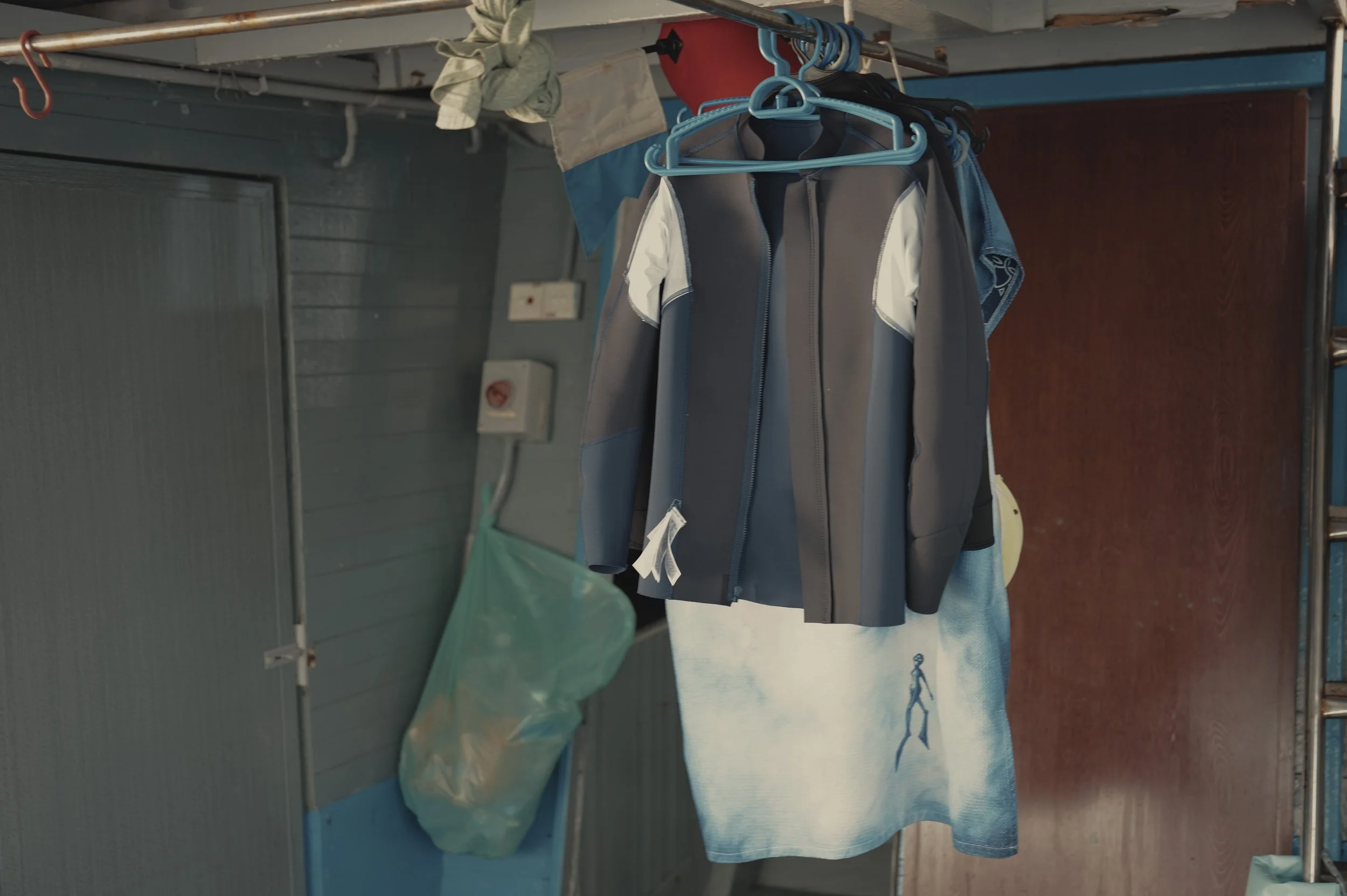 Clothes hanging on a rack in a laundry room, with a towel and a jacket visible.