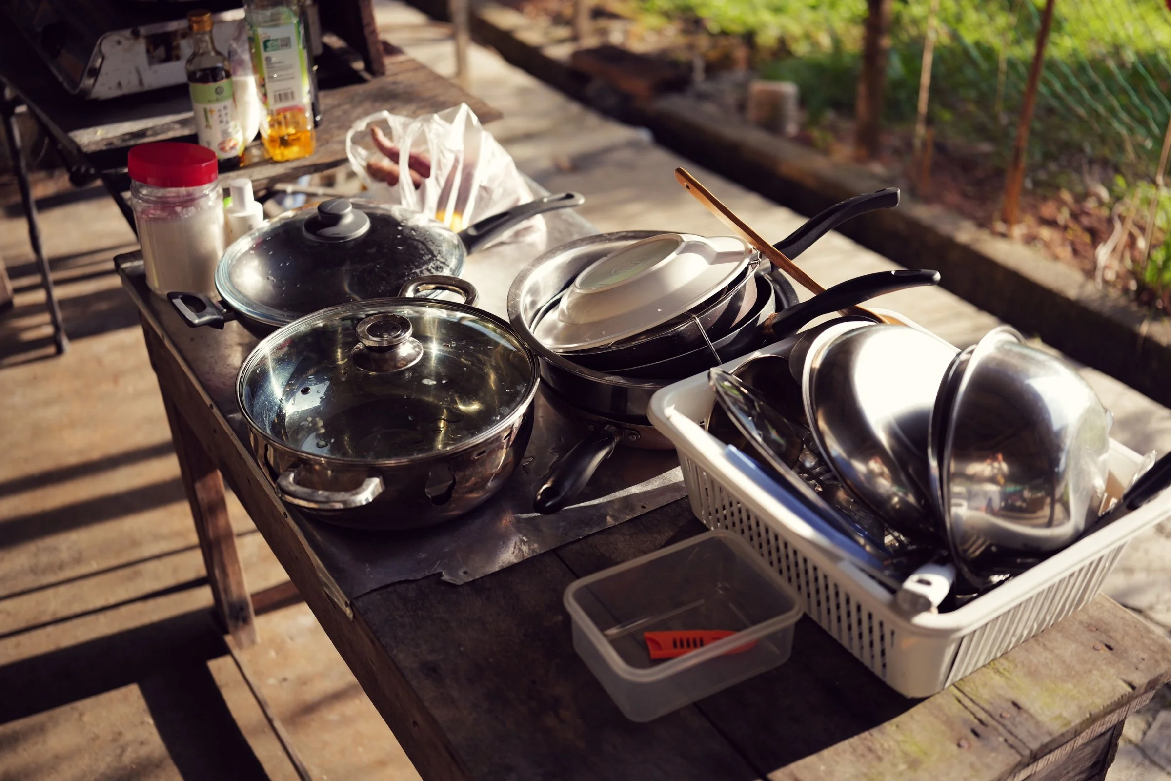 Metal bowls and cookware catch warm sunlight on a campsite table.