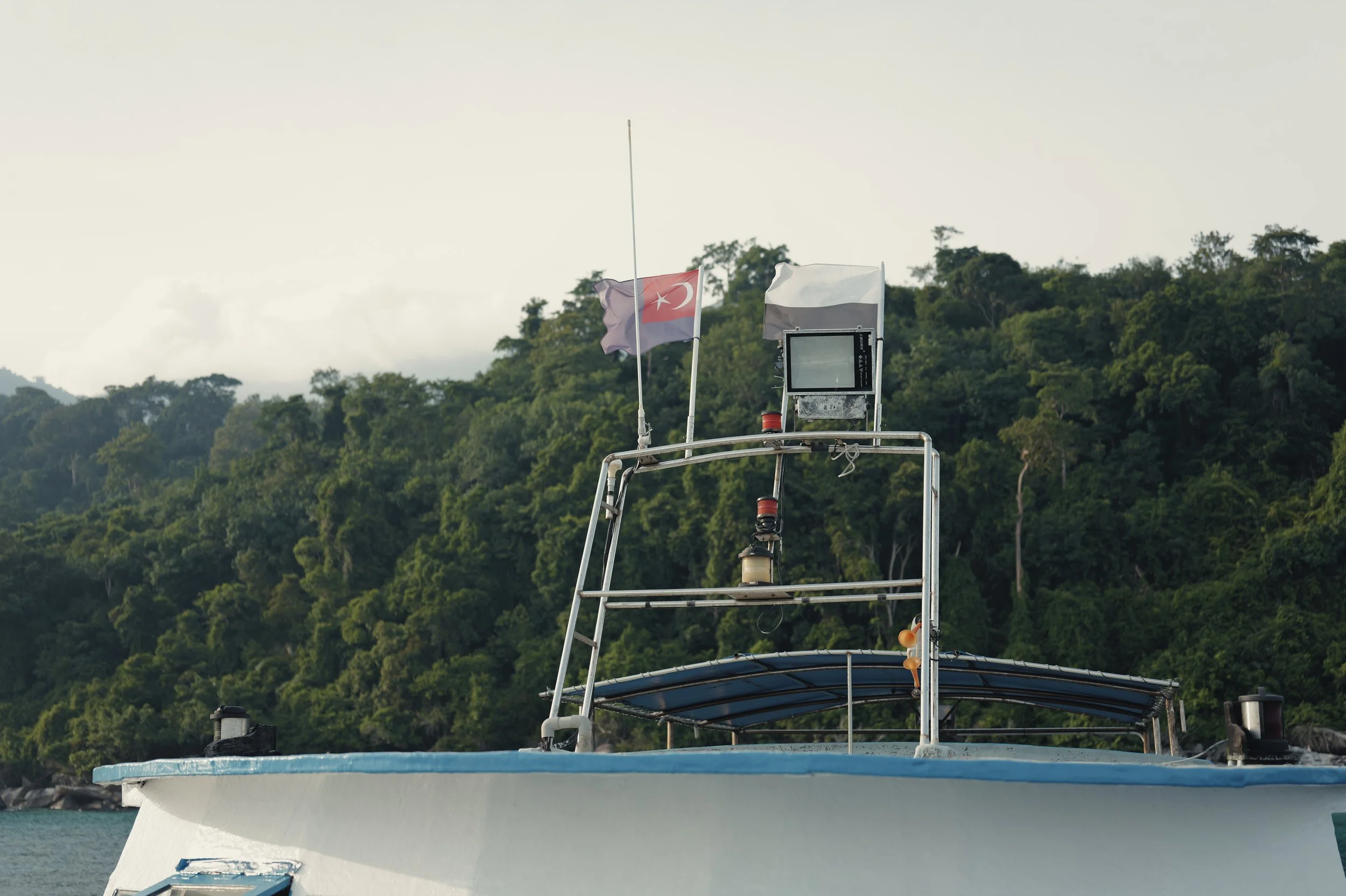 Boat deck with flags, including a Turkish flag, against a backdrop of green, forested hills.