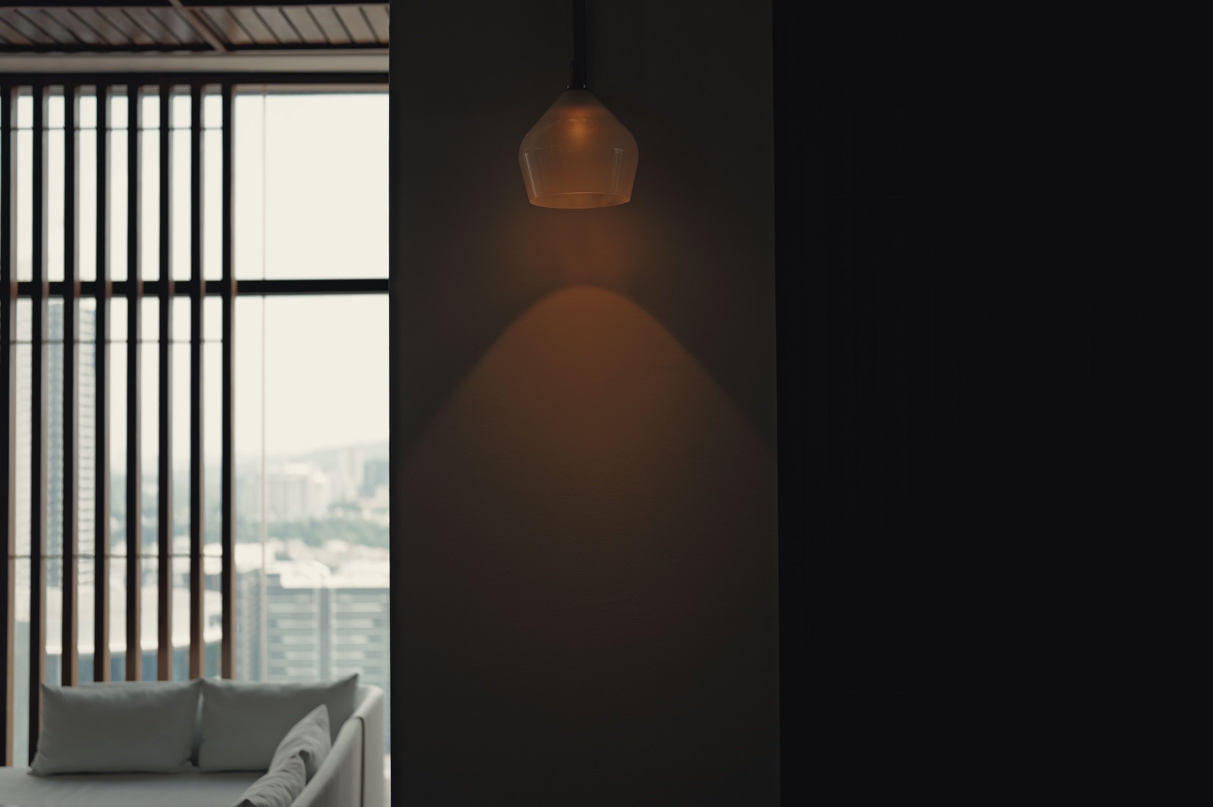 An amber wall lamp glows beside a barred window and a pale chair.