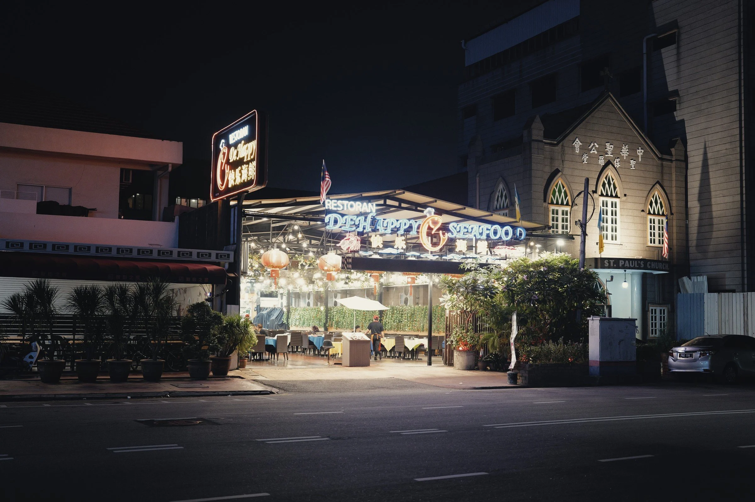 An illuminated food-court entrance glows across a quiet road at night.