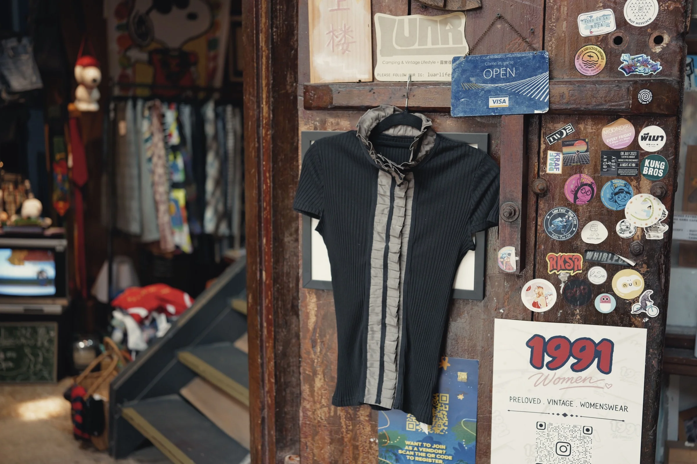 A black T-shirt hangs on a weathered wooden door covered with stickers.