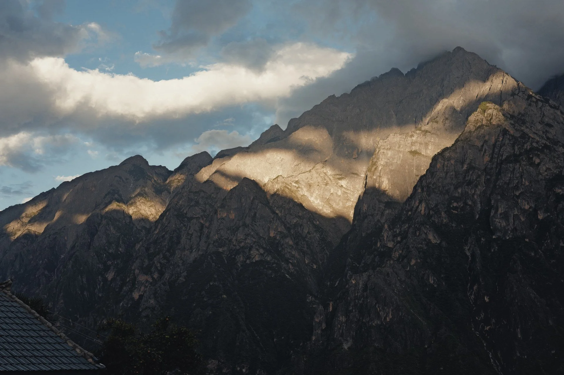 Late-afternoon sunlight illuminating the mountain ridges above Tiger Leaping Gorge, viewed from Qi Feng Shan Homestay.