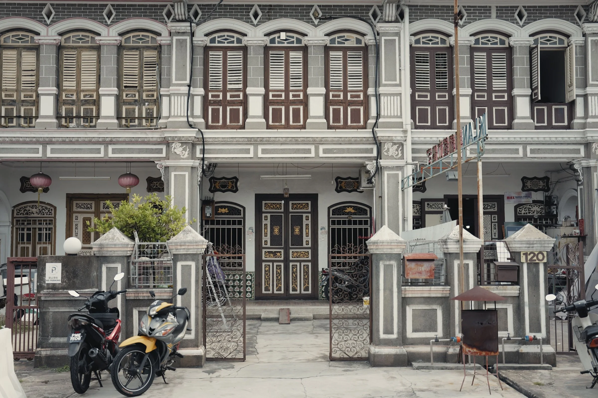 Decorative shutters and carved doors line a historic shophouse facade.