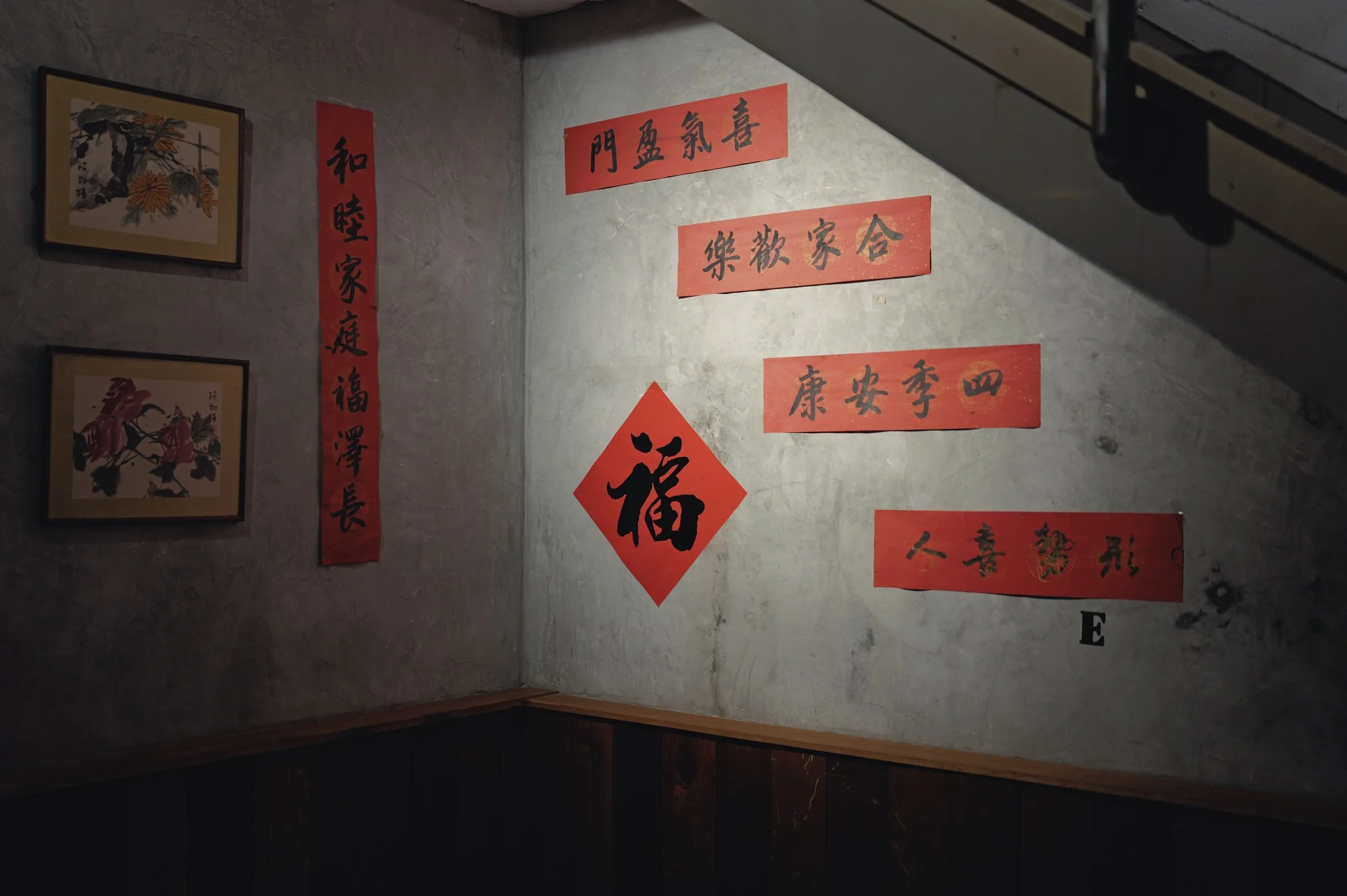 Red calligraphy slips cover a textured wall beneath a staircase.