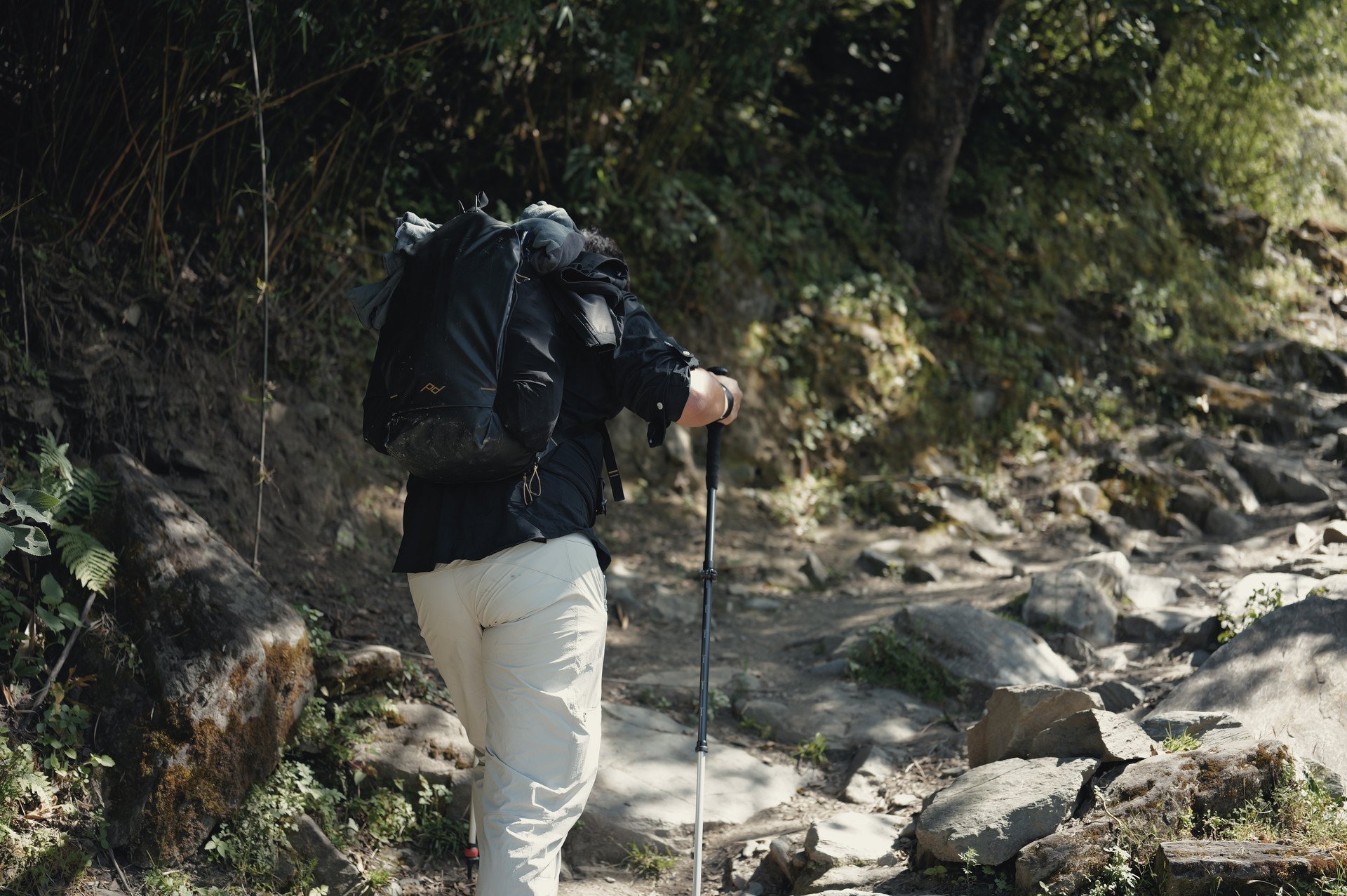A hiker with a backpack climbing the rocky High Trail at Tiger Leaping Gorge, Yunnan.