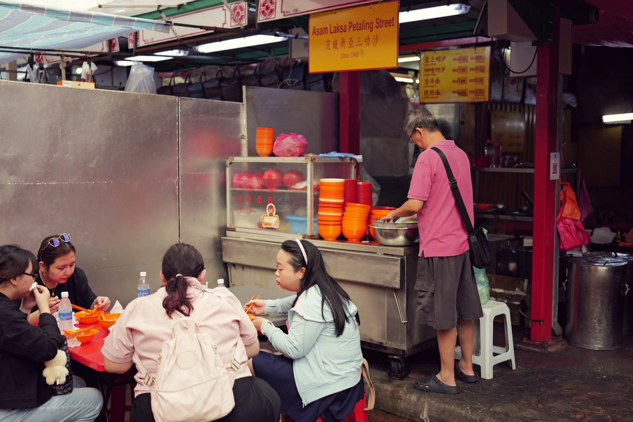 Diners gather at a small table beside a busy street-food stall.