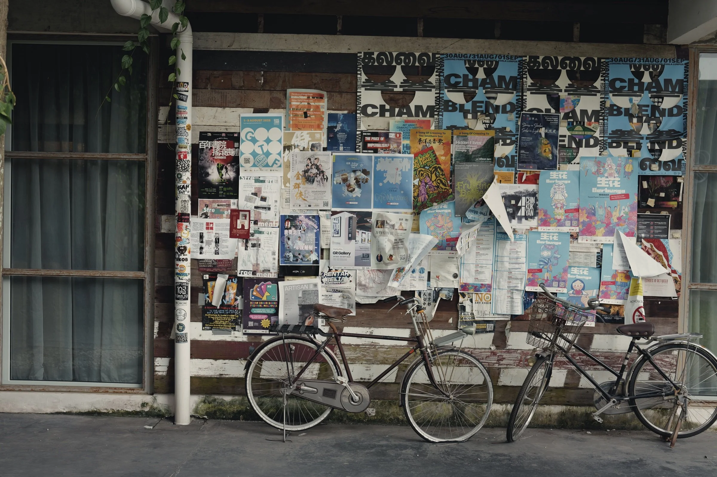 Two bicycles lean against a wall covered with colourful posters.