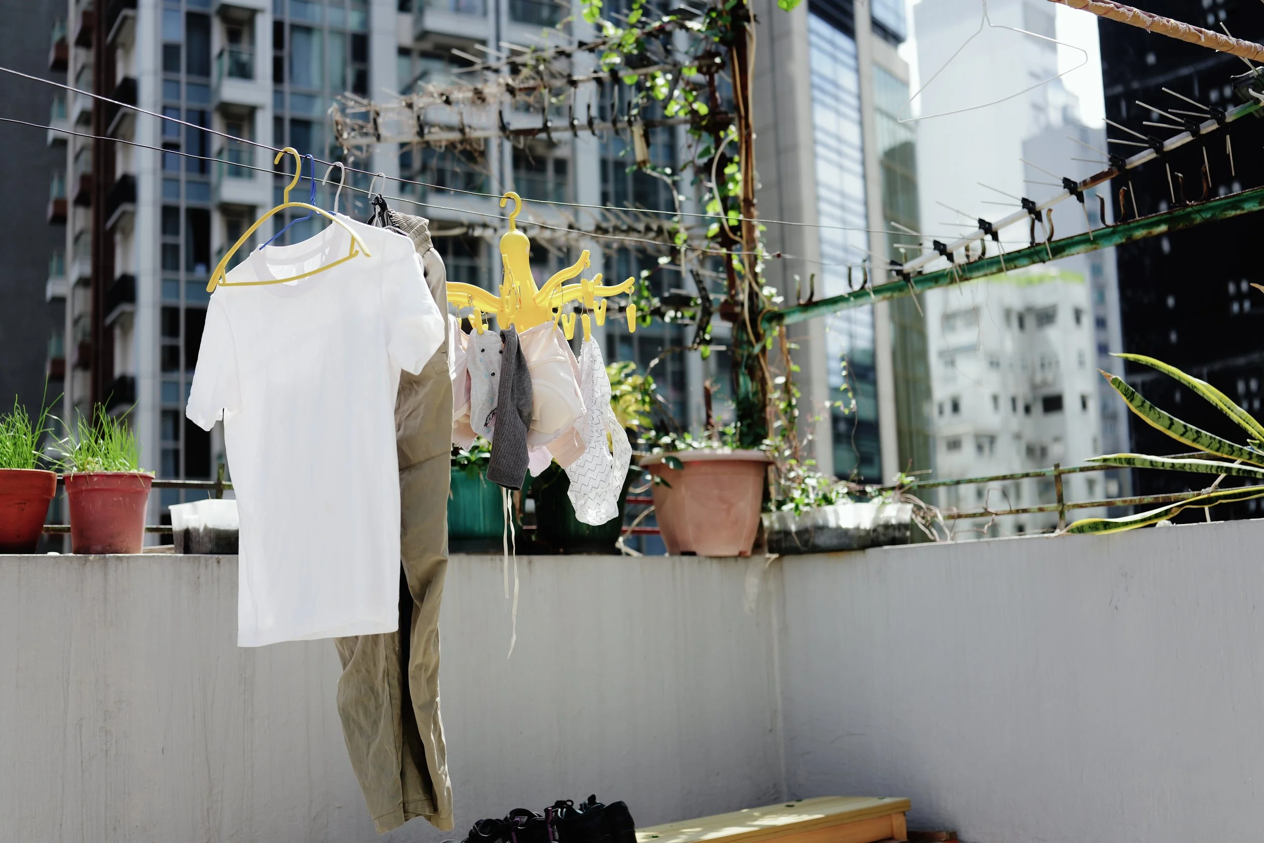 Clothes hanging on a line on a balcony with potted plants and buildings in the background.
