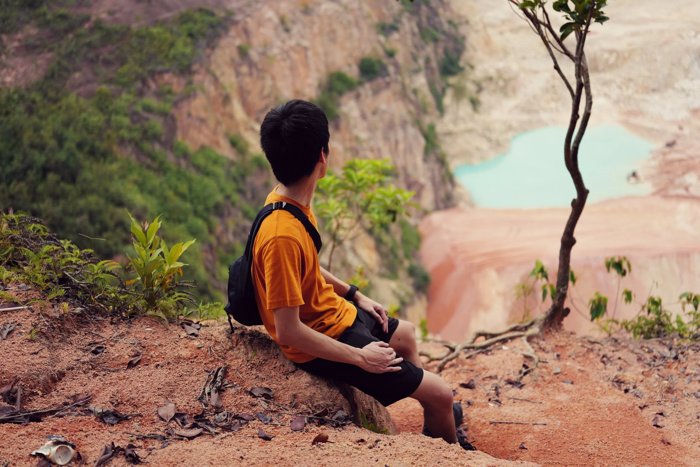 A hiker in a yellow shirt sits above the turquoise quarry pool.