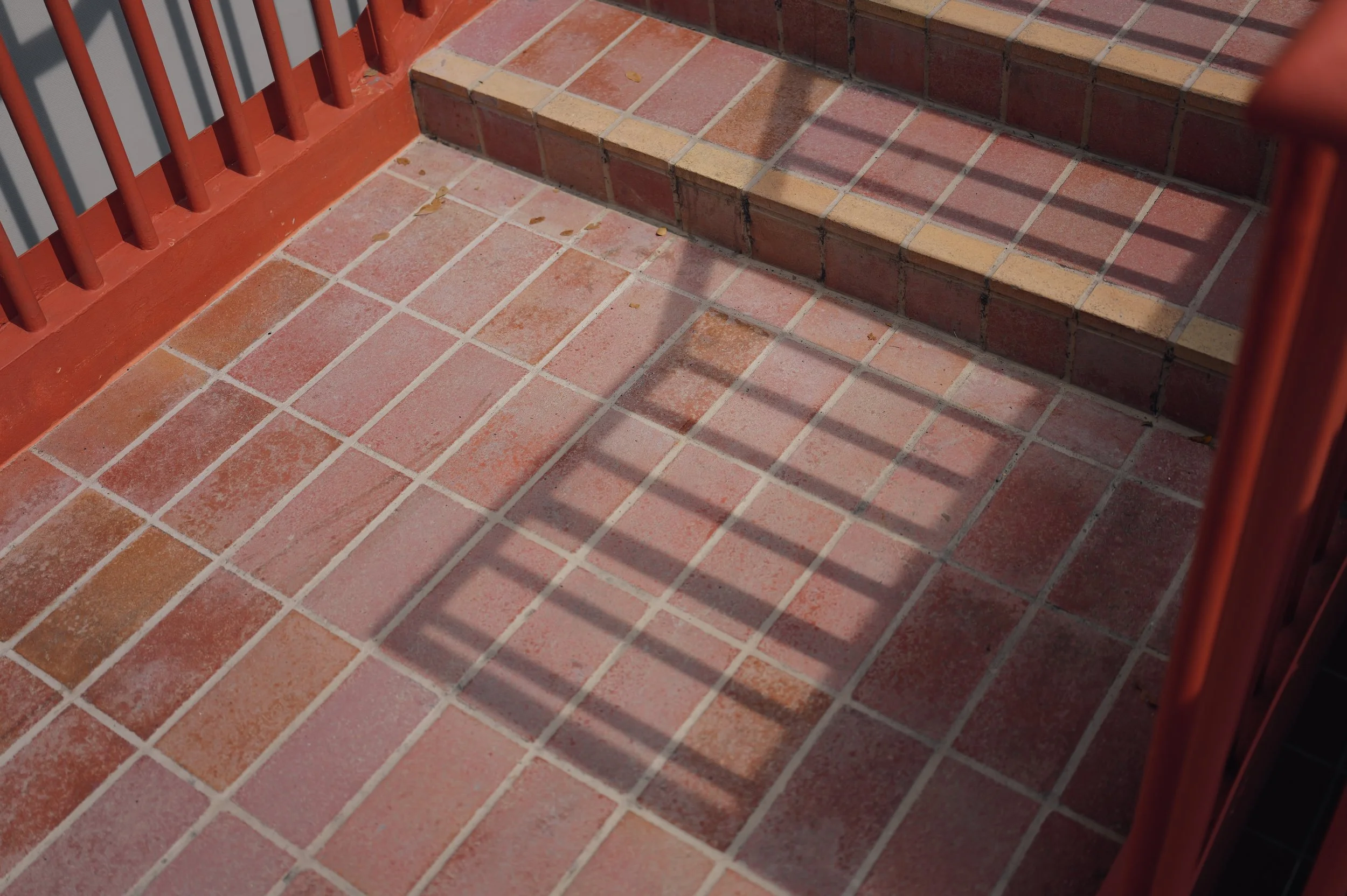Brick steps with a red railing and a tiled floor with some leaves.