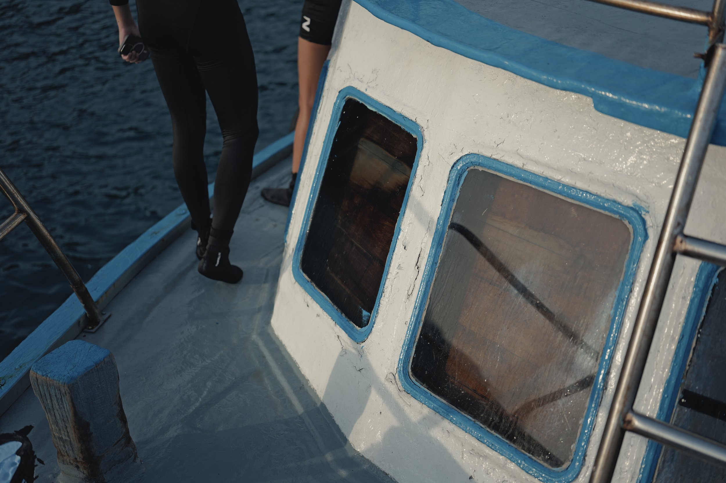 Close-up of the side of a boat with small rectangular windows, painted white with blue trim, and a person standing nearby on the deck.