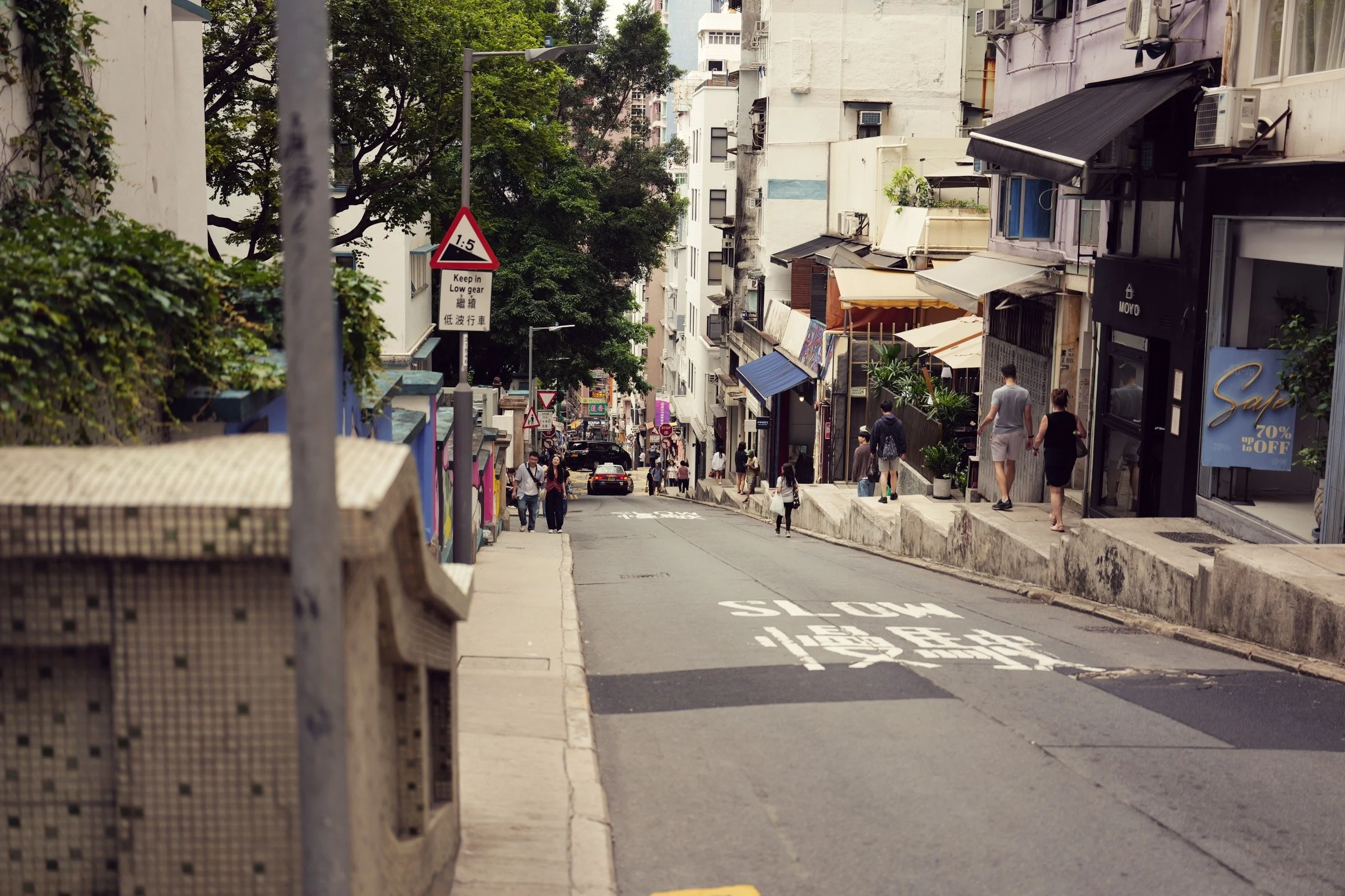 Pedestrians and shopfronts along a steep hillside street in Central, Hong Kong, photographed with a Leica Q3 43.