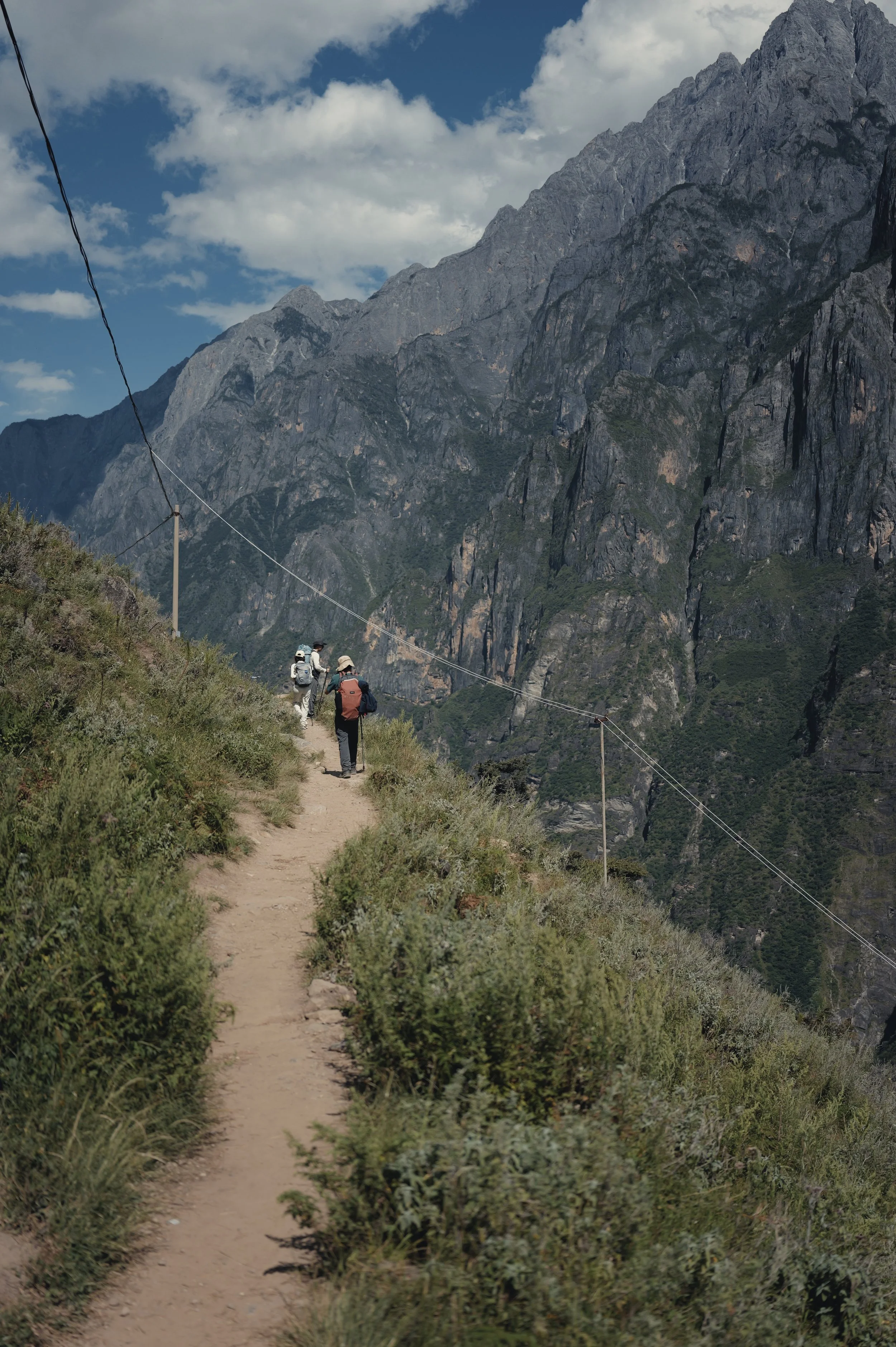 Hiker on a narrow path below towering cliffs in Tiger Leaping Gorge