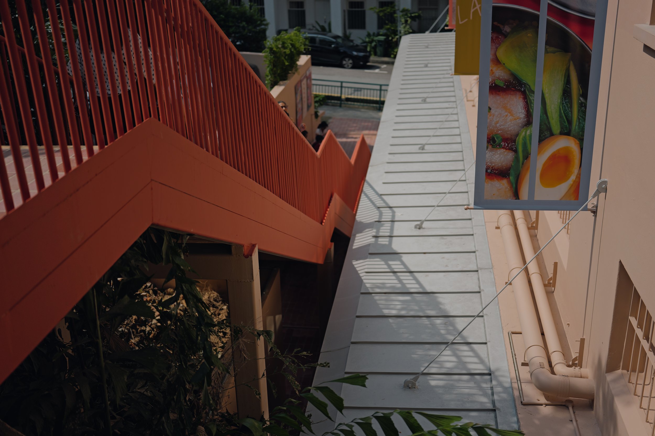 Outdoor stairway with orange railing and white steps, adjacent to a building with a sign displaying produce such as strawberries, kiwi, and eggs.