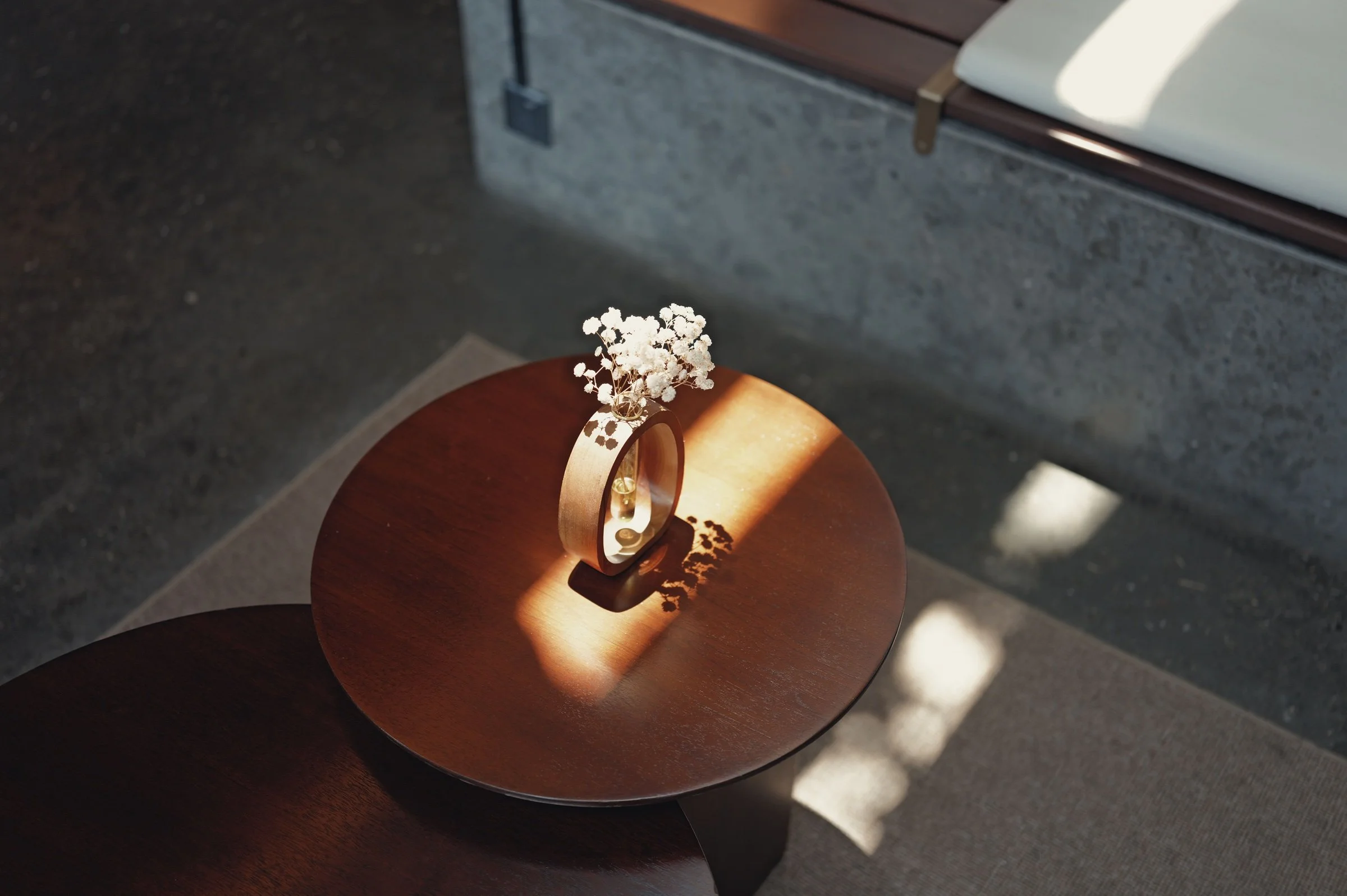 Dried flowers in a vase catch a strip of sunlight on a round wooden table.