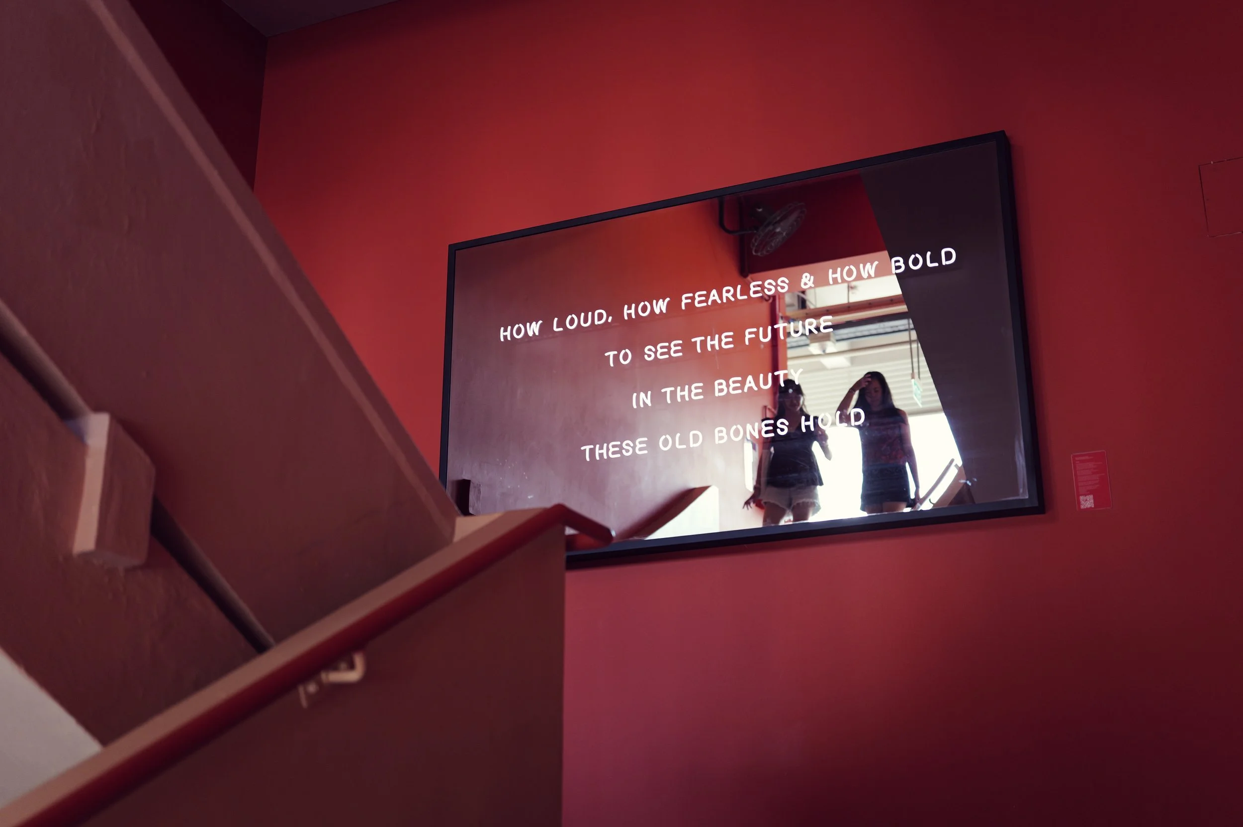 A mirror displaying a quote on a red wall, with two women visible in the mirror's reflection.