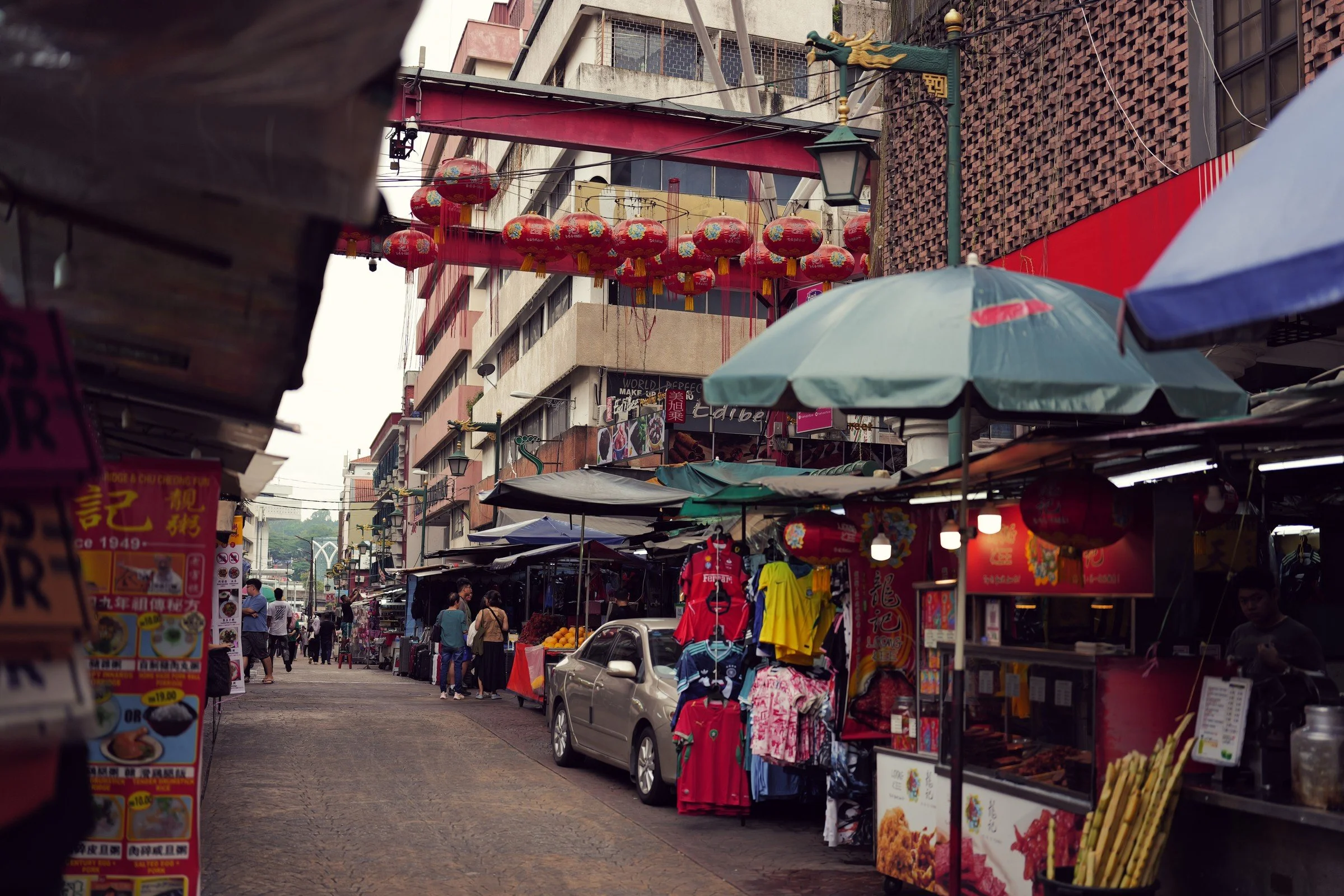 Umbrellas and stalls line a narrow shopping street beneath red lanterns.