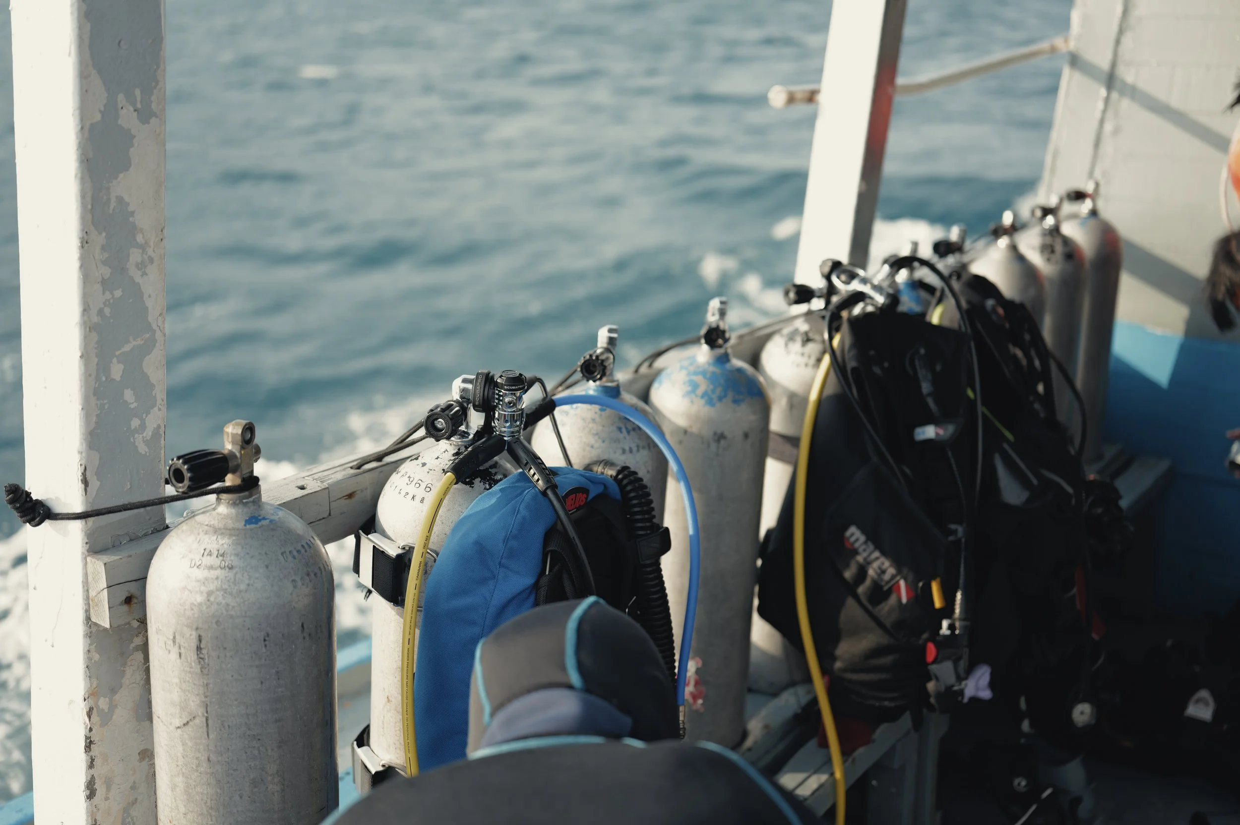 Diving equipment secured to the side of a boat, with compressed air tanks and wetsuits, on the open water.