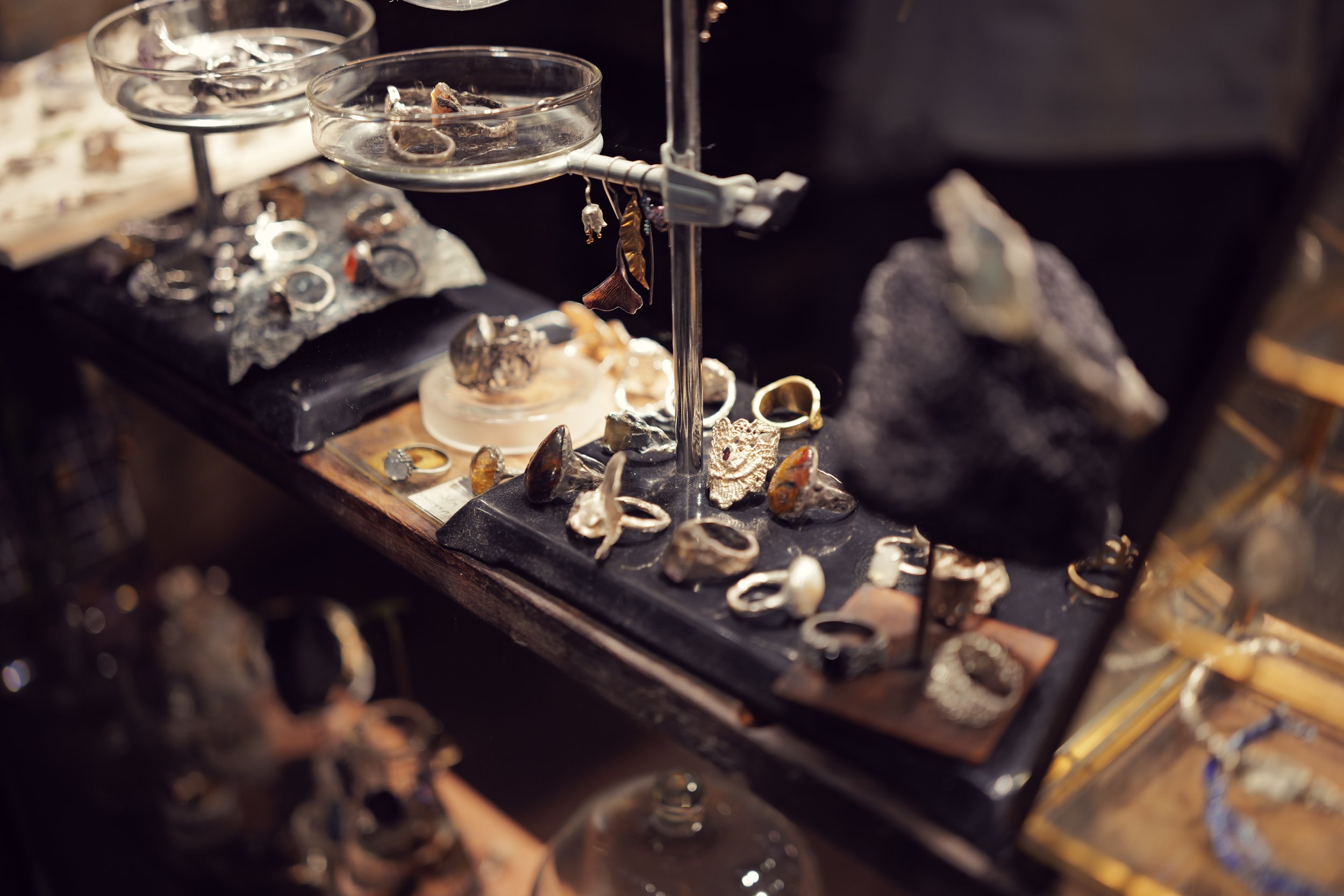 Close-up of jewelry display with rings, necklaces, and earrings on black velvet and glass trays.