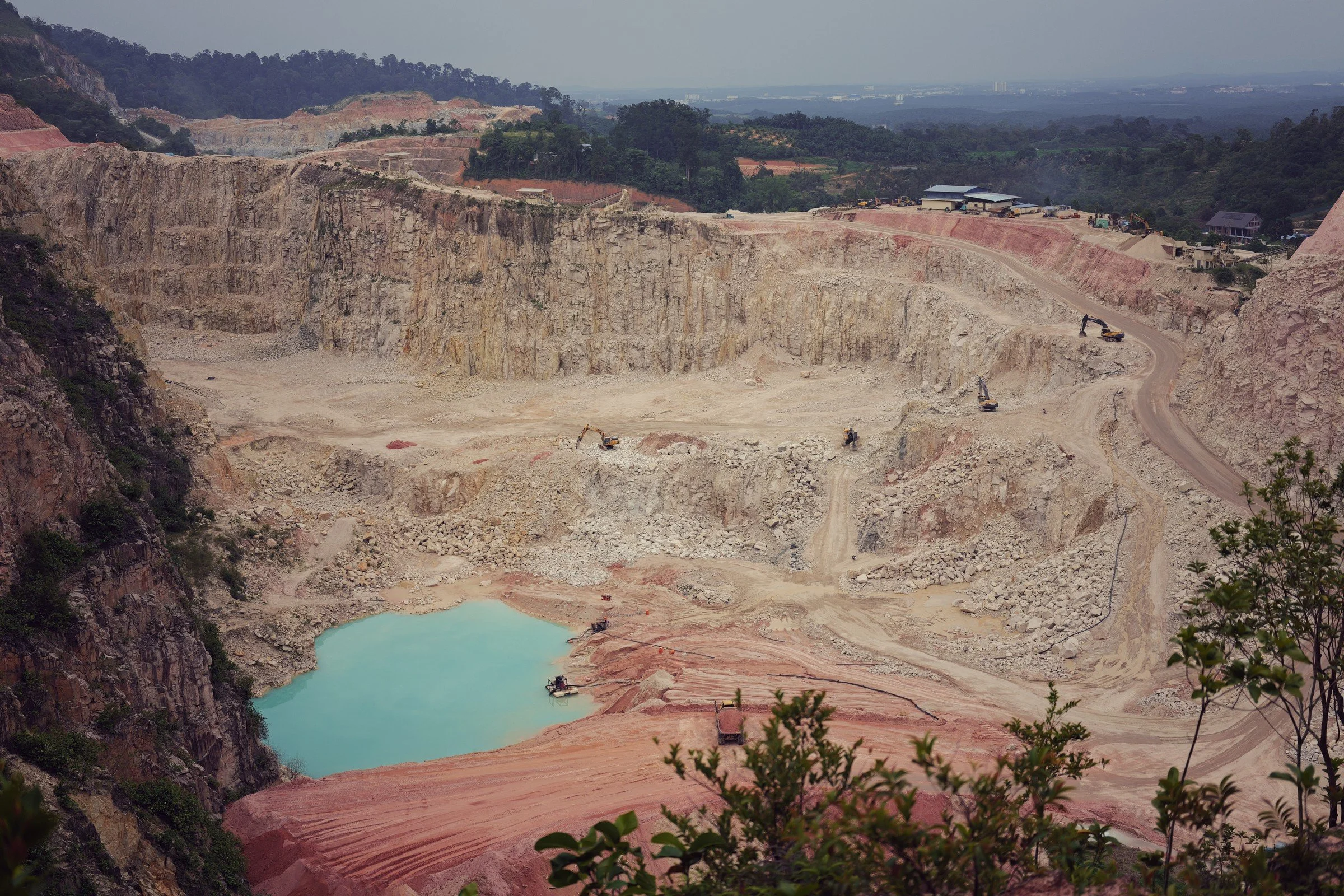 Turquoise water sits below pale quarry walls and red earth, with distant hills beyond.