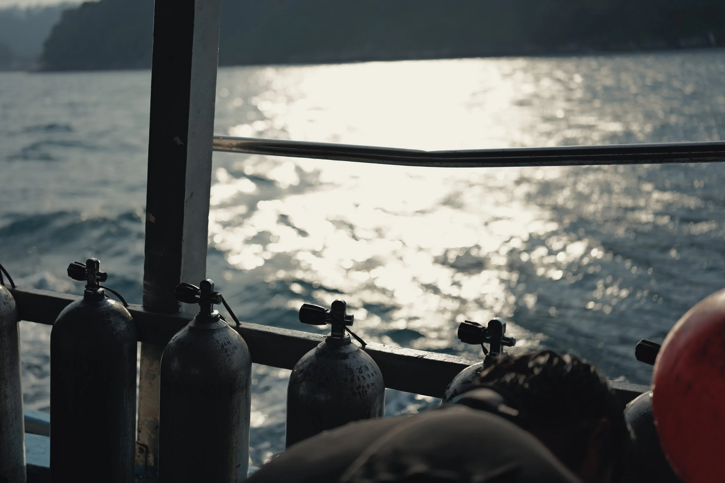 View of a boat's railing with scuba tanks, looking out over the water with sunlight reflecting off the surface.