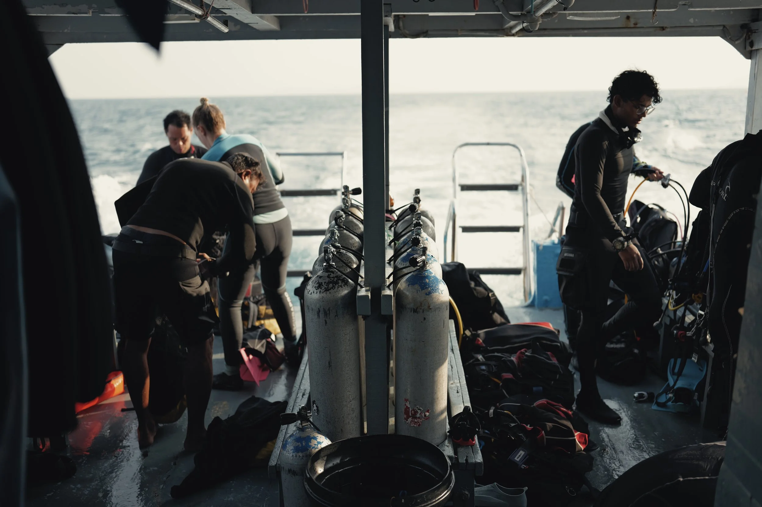 People preparing scuba gear on a boat with the ocean in the background.