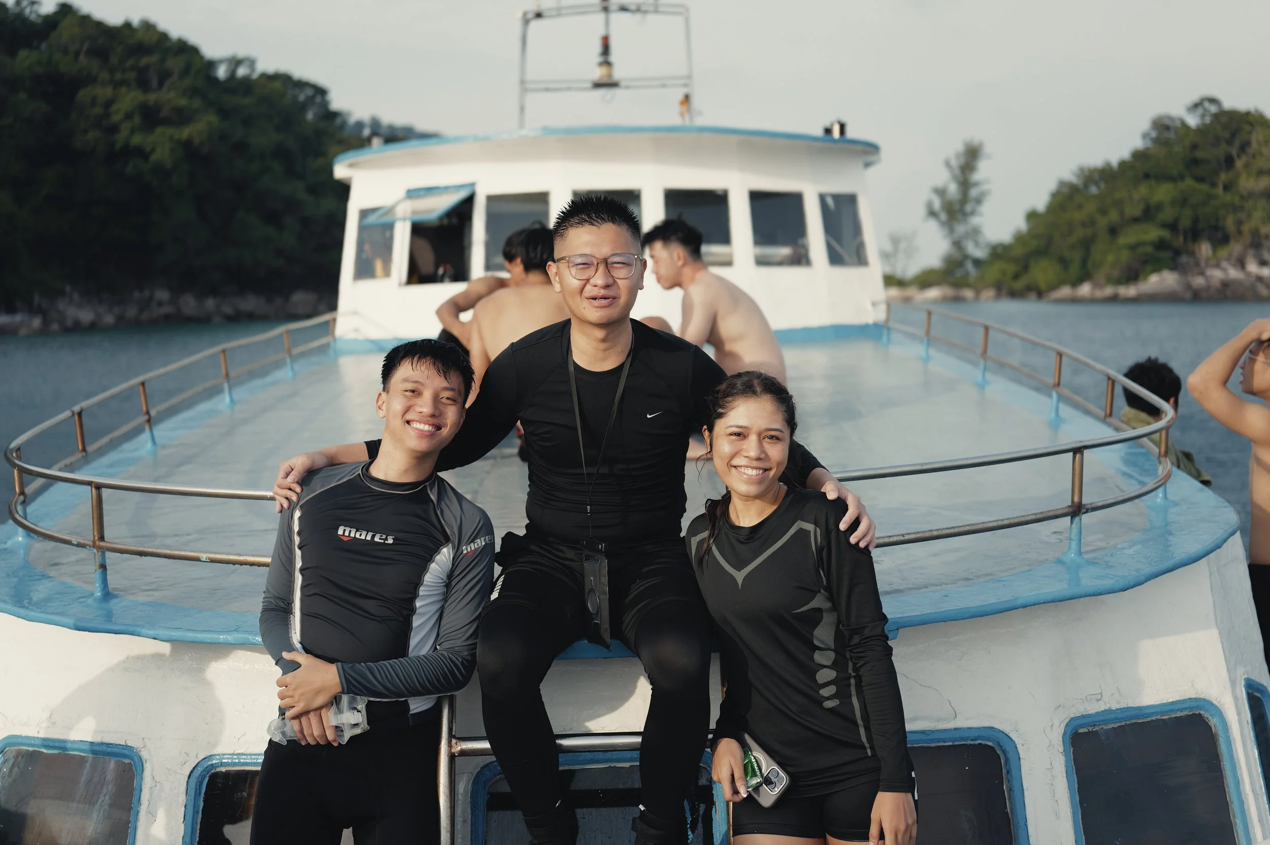 Group of four young adults smiling and posing on the deck of a boat with water and trees in the background.