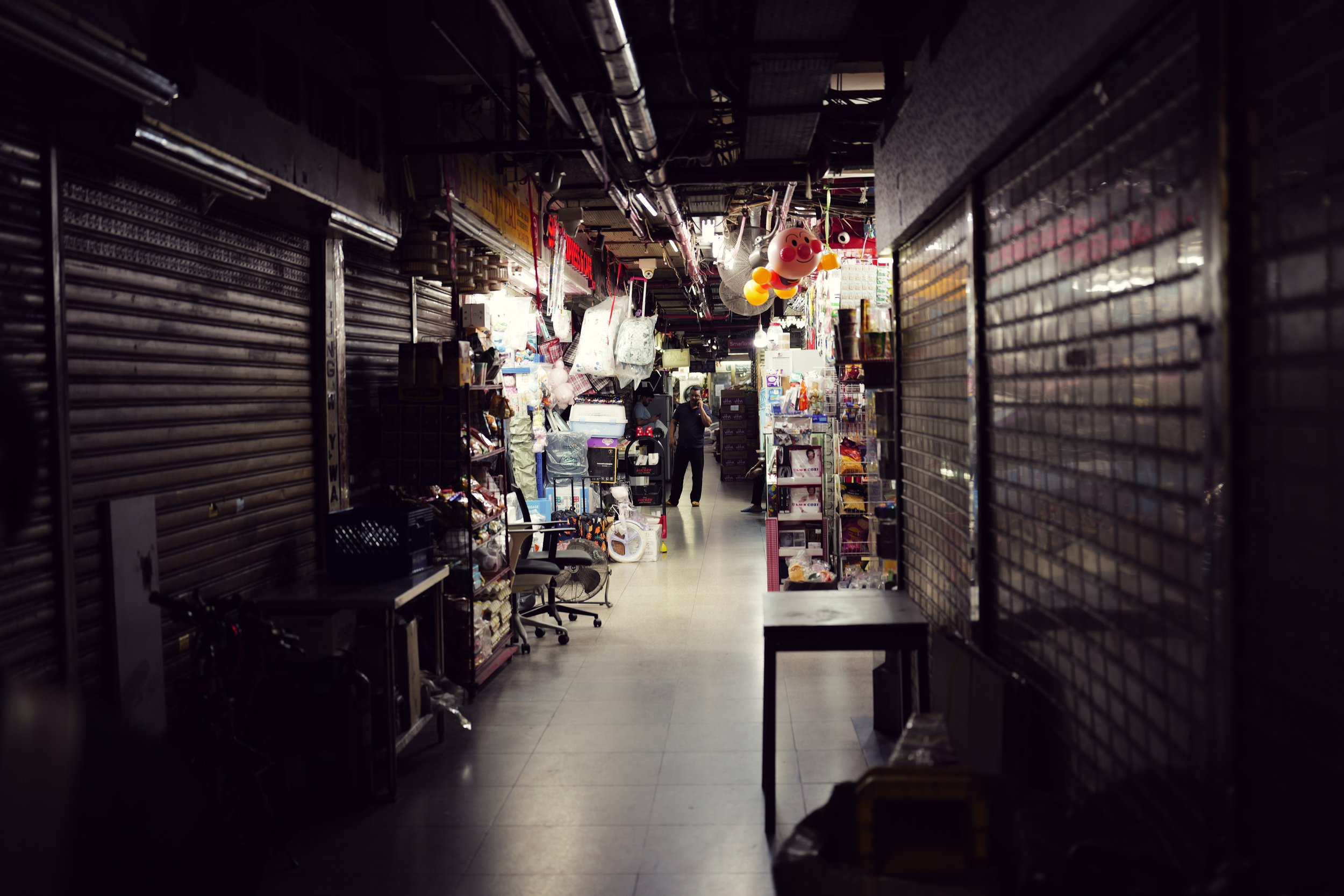 Empty store aisle with shelves on both sides, some items on display, and a person standing in the distance, talking on the phone.