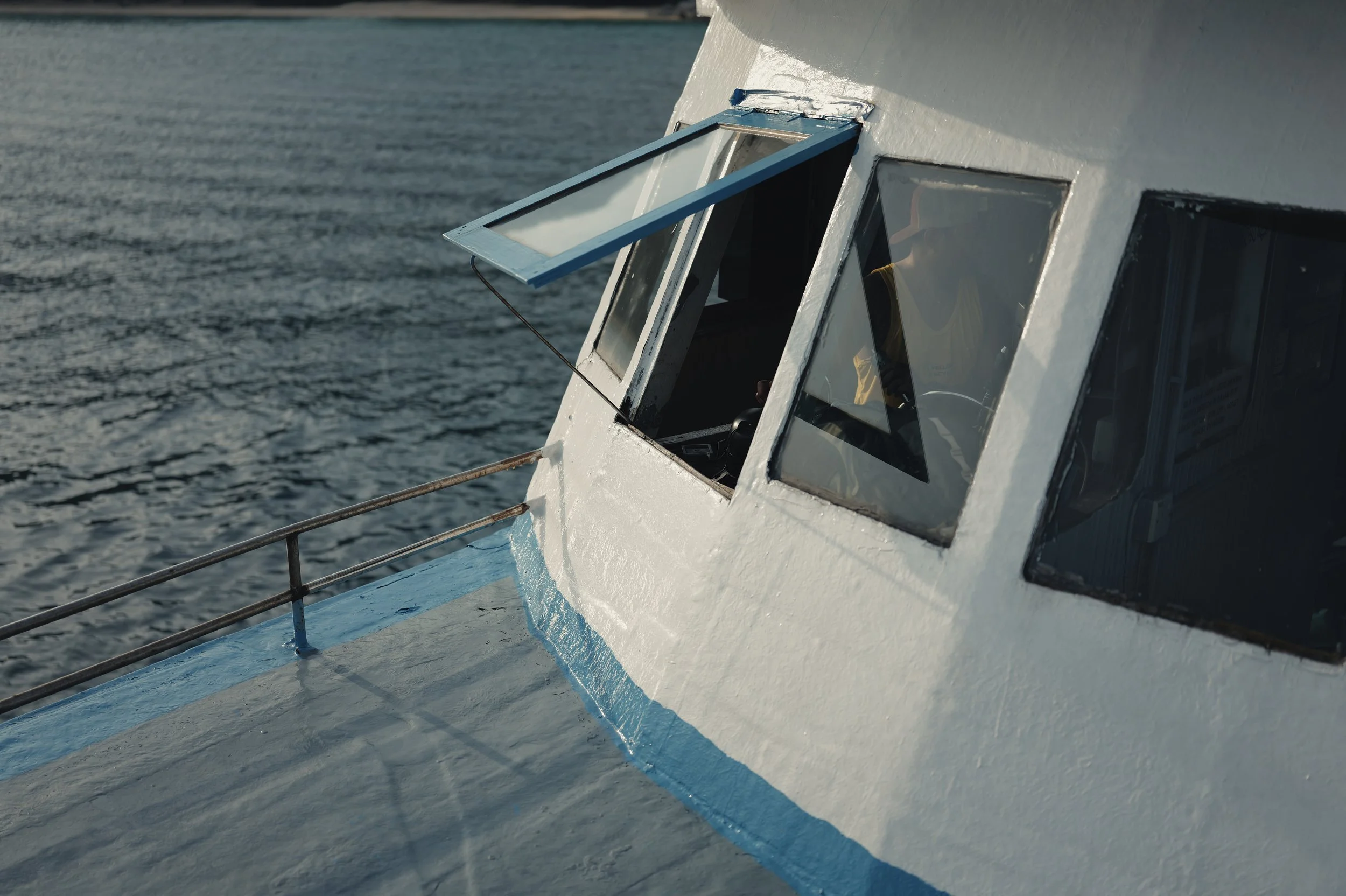 Close-up of a ship's bridge with an open window and water surrounding the vessel.