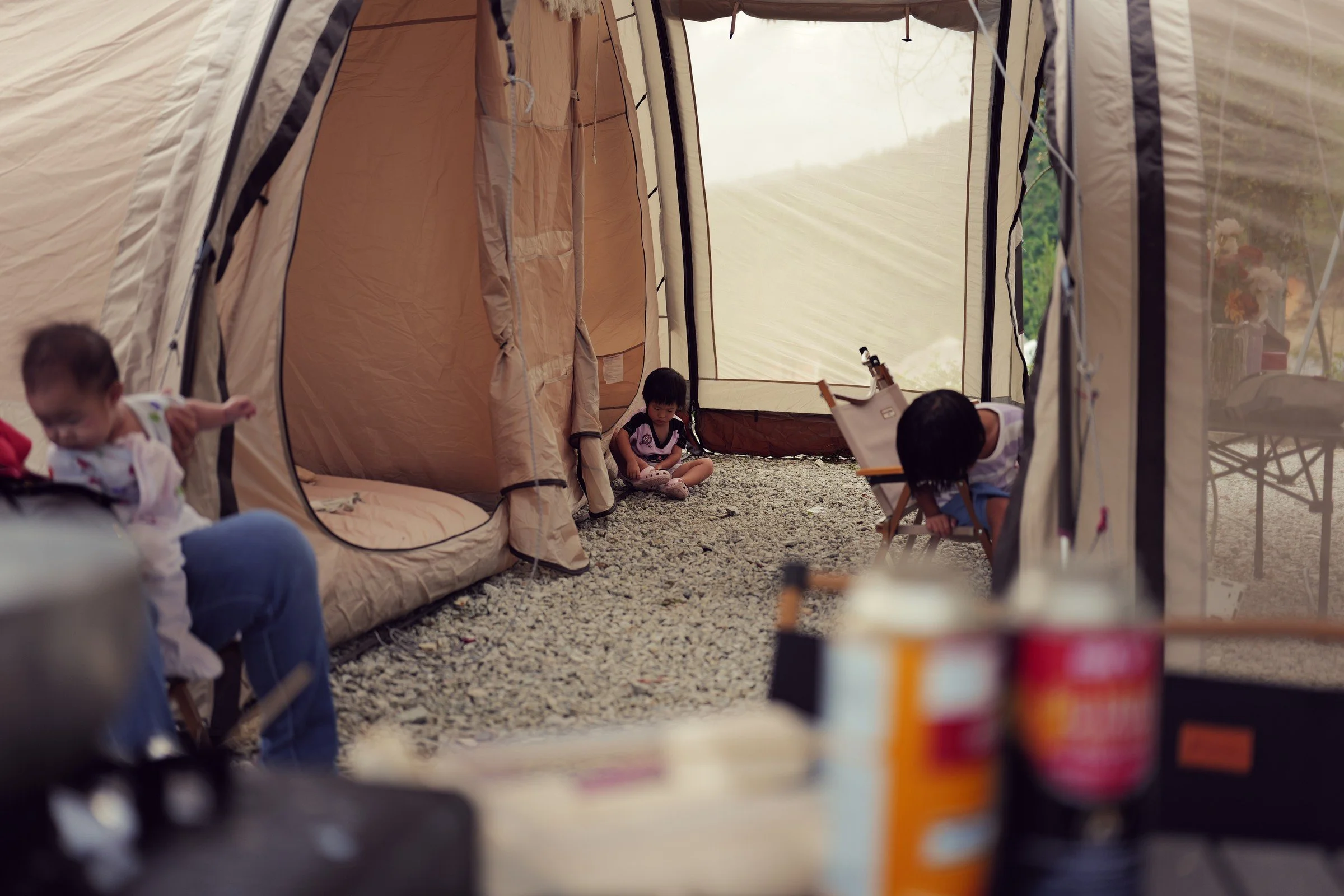 Children play between canvas tents on a gravel campsite.
