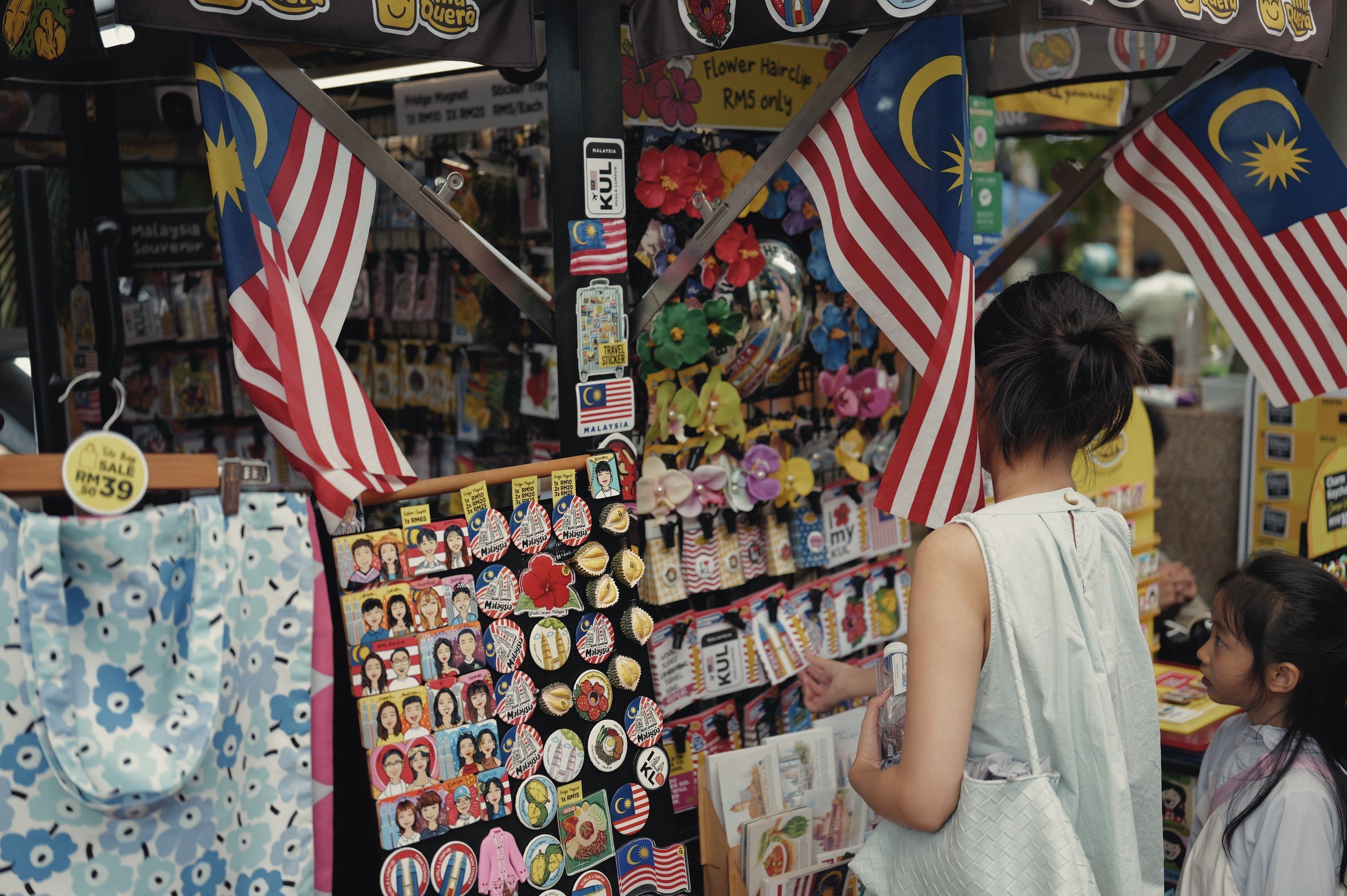 A shopper browses a colourful souvenir stall hung with Malaysian flags.