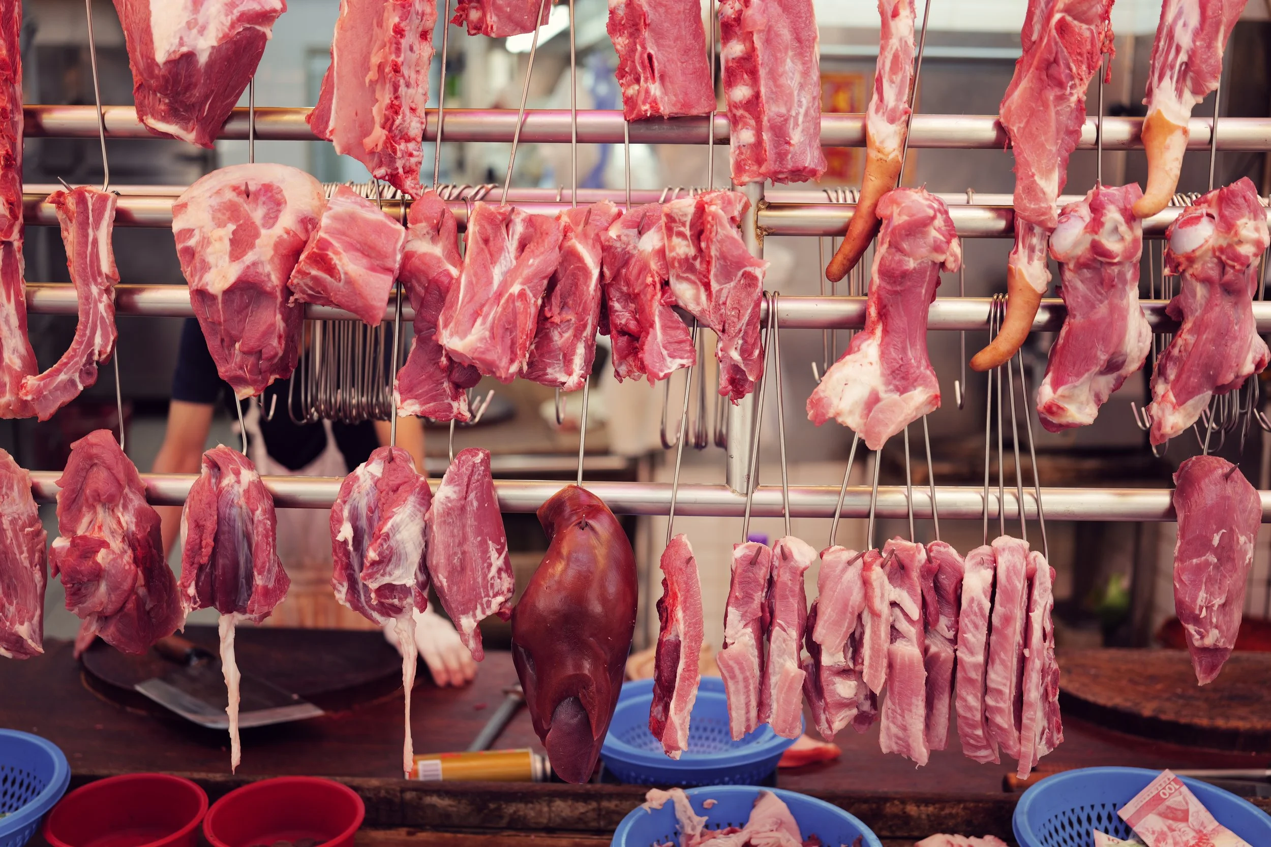 Various cuts of raw meat hanging on metal hooks at a butcher shop or market stall.
