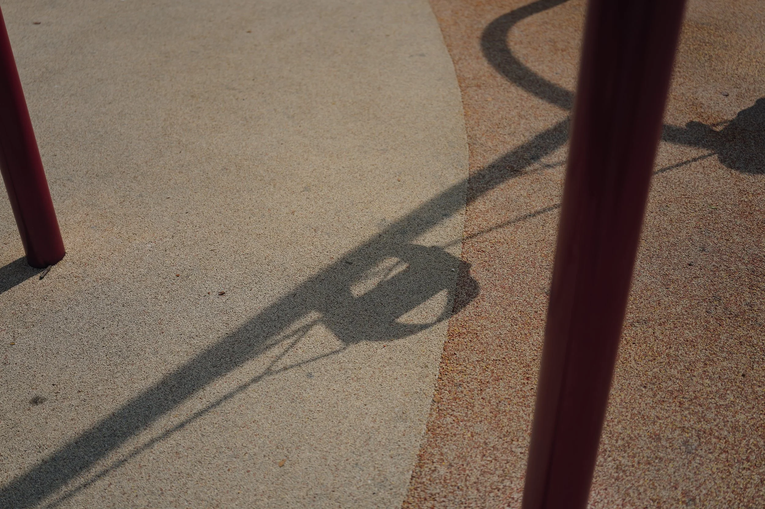 Close-up of the shadow of red metal bars on beige and reddish-brown textured concrete ground.