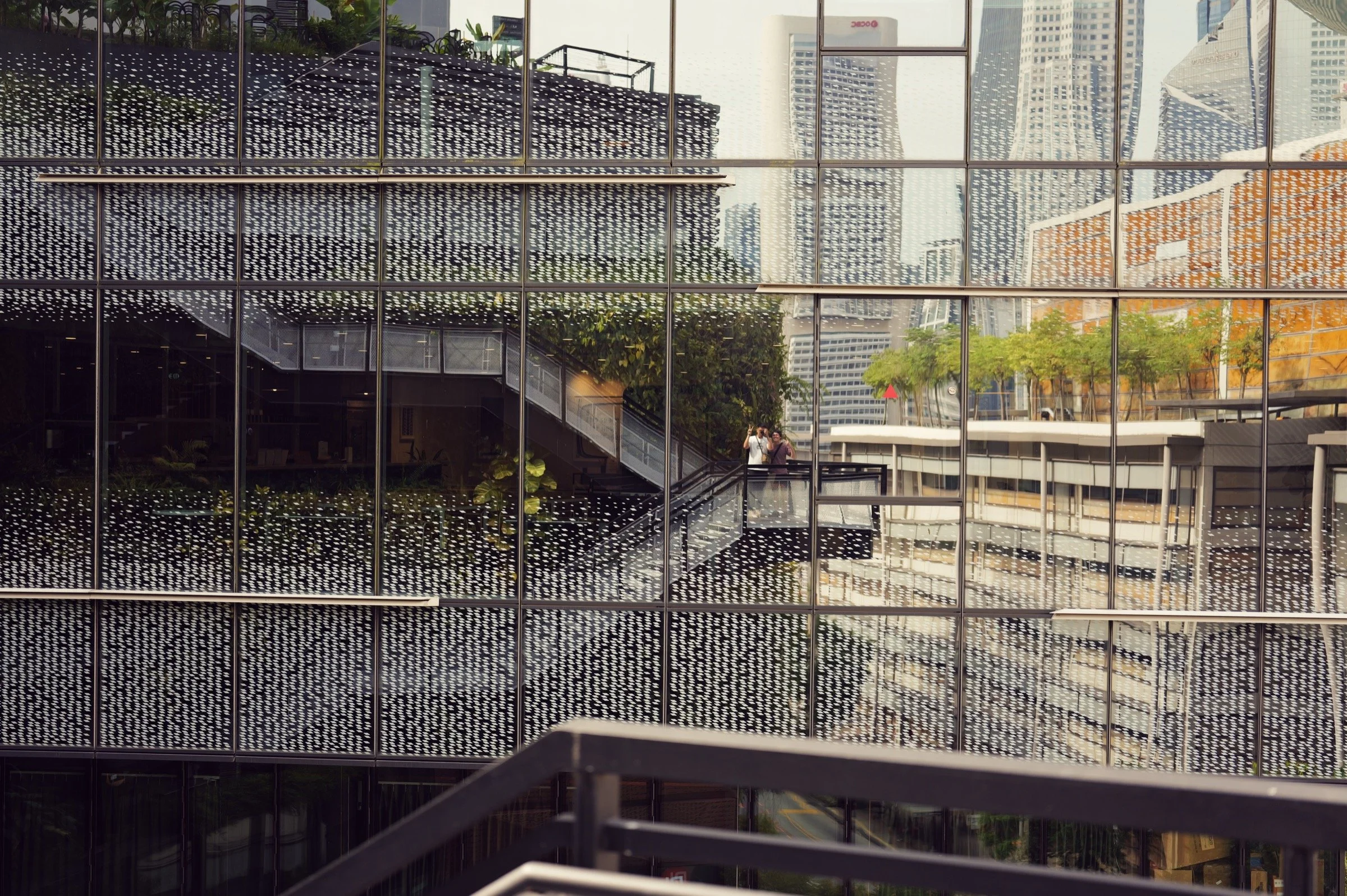 Layered mesh screens, planted terraces and distant towers form a city rooftop view in Singapore.