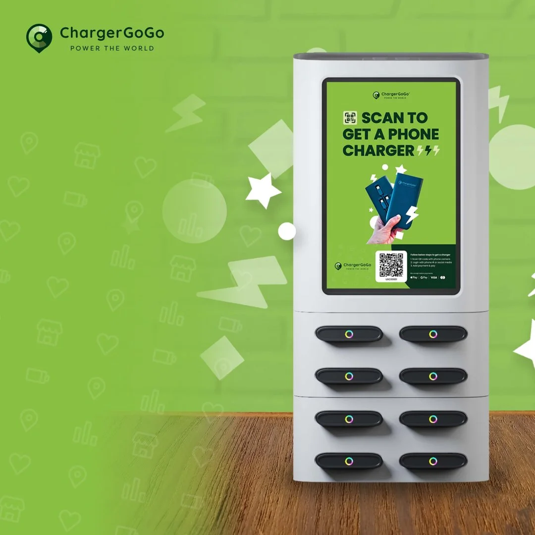 A white kiosk with a digital screen advertising ChargerGoGo, offering phone chargers accessible via QR code, with a wooden surface at the base and a green wall background featuring subtle design icons.