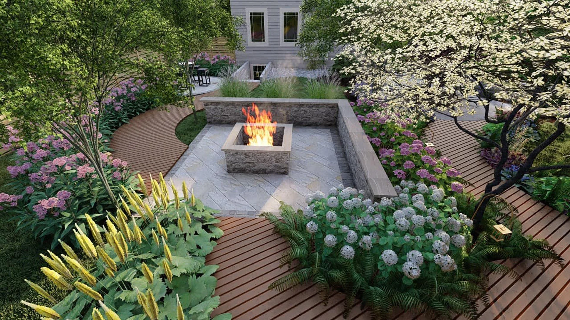 A backyard garden with a stone fire pit at the center, surrounded by a curved wooden deck and lush flowering plants including pink and white flowers, green trees, and shrubs, with a house in the background.