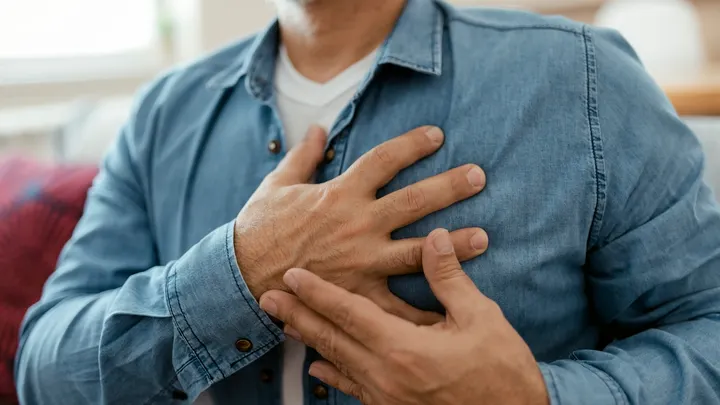 Person wearing a denim shirt holding their chest with one hand.