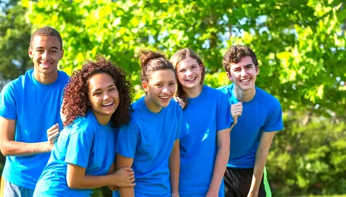 Grupo de jóvenes sonriendo y vestidos con camisetas azules en un parque con árboles verdes.