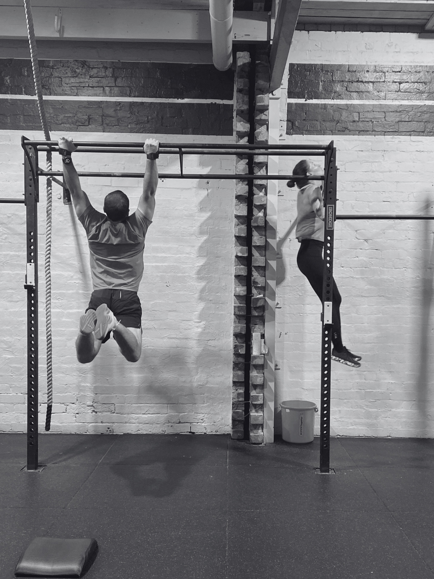 Two people completing kipping pull ups on rig